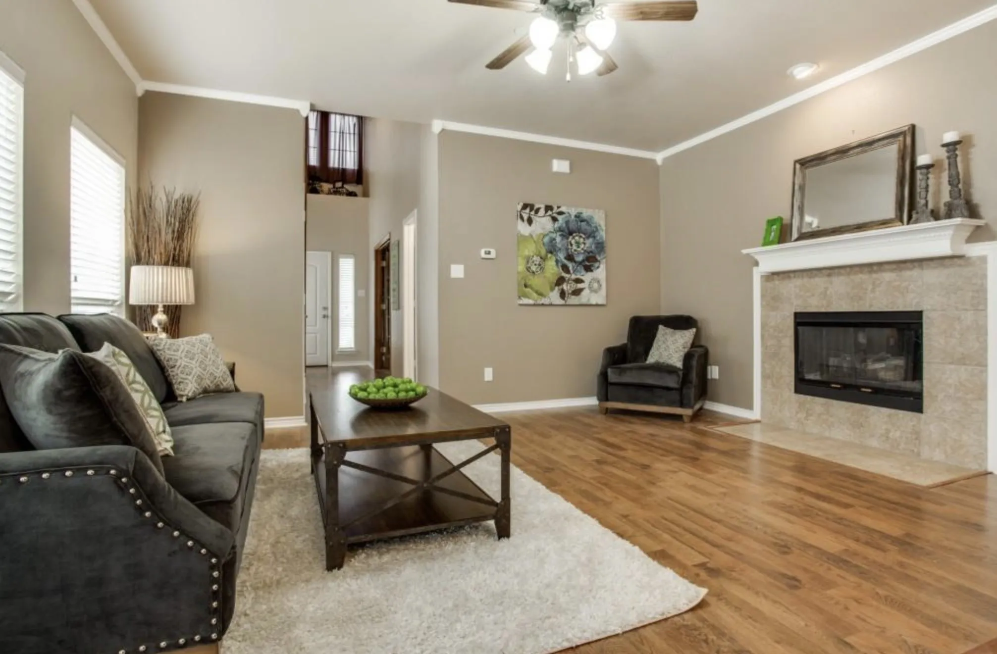 Living area featuring wood-finish flooring, a ceiling fan, a fireplace with a tile surround and white mantel, and crown molding