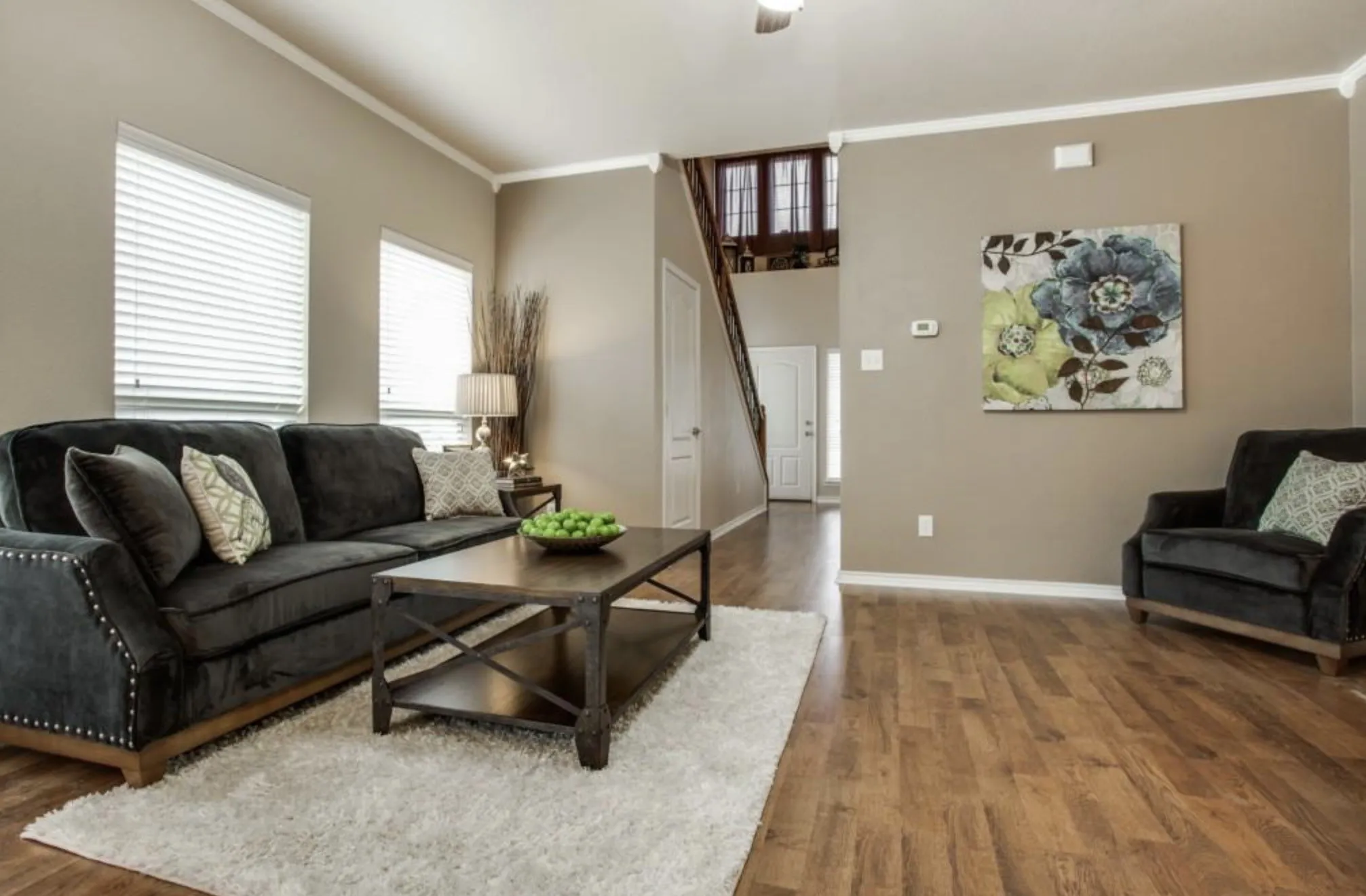Wood-finish flooring, neutral wall paint, white crown molding, multiple windows with blinds, and visible staircase to an upper level