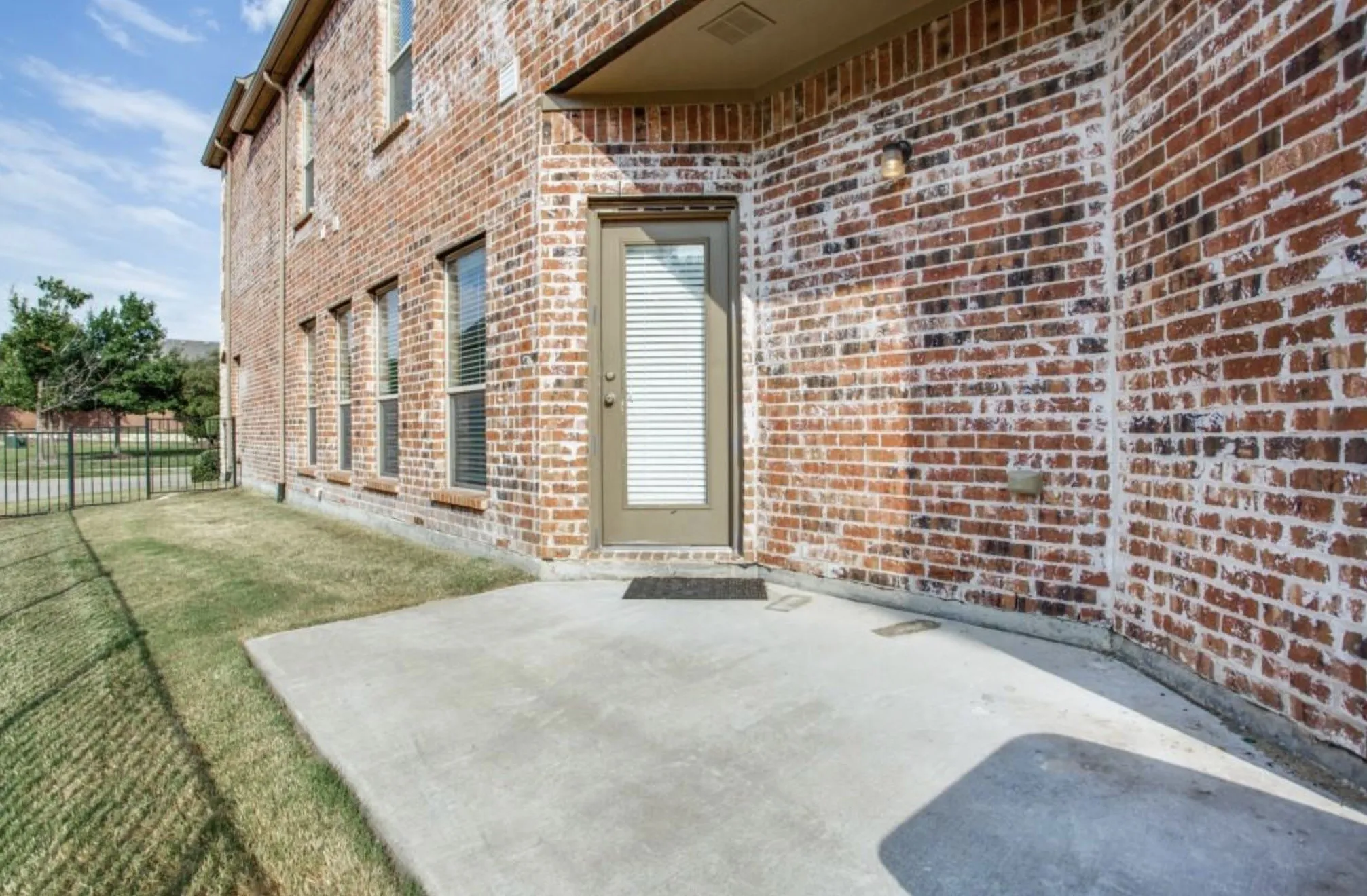Brick exterior with multiple windows, a concrete patio, and a fenced yard
