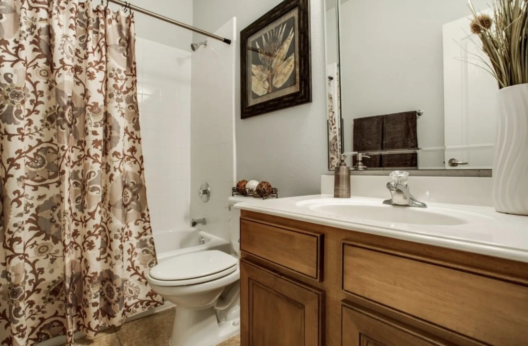 Bathroom featuring a single vanity with wood-finish cabinetry, a white countertop with an integrated sink, a large wall-mounted mirror, and a white tub with shower