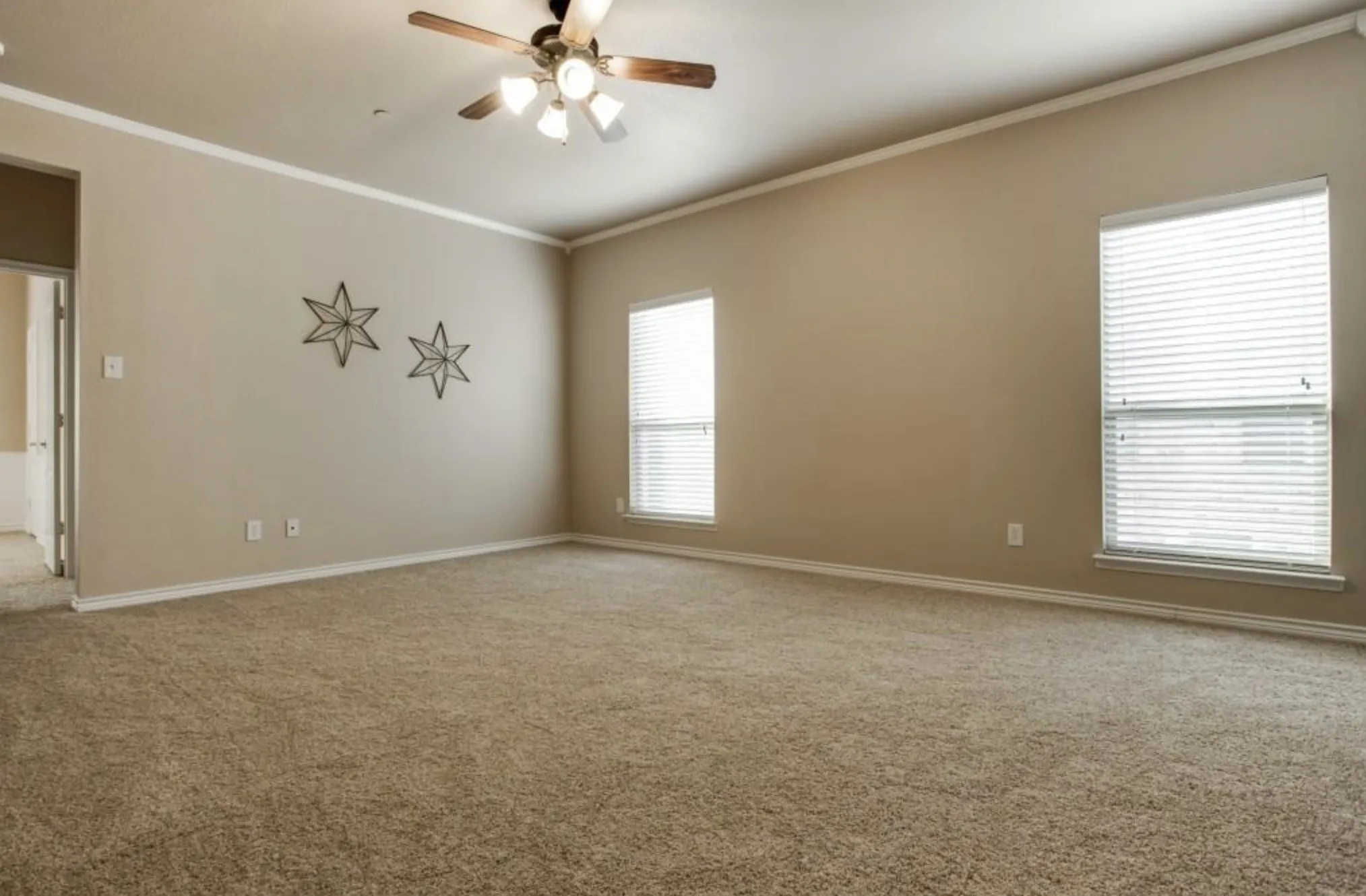 Spacious room featuring neutral carpeting, crown molding, a ceiling fan with integrated lighting, and multiple windows with blinds