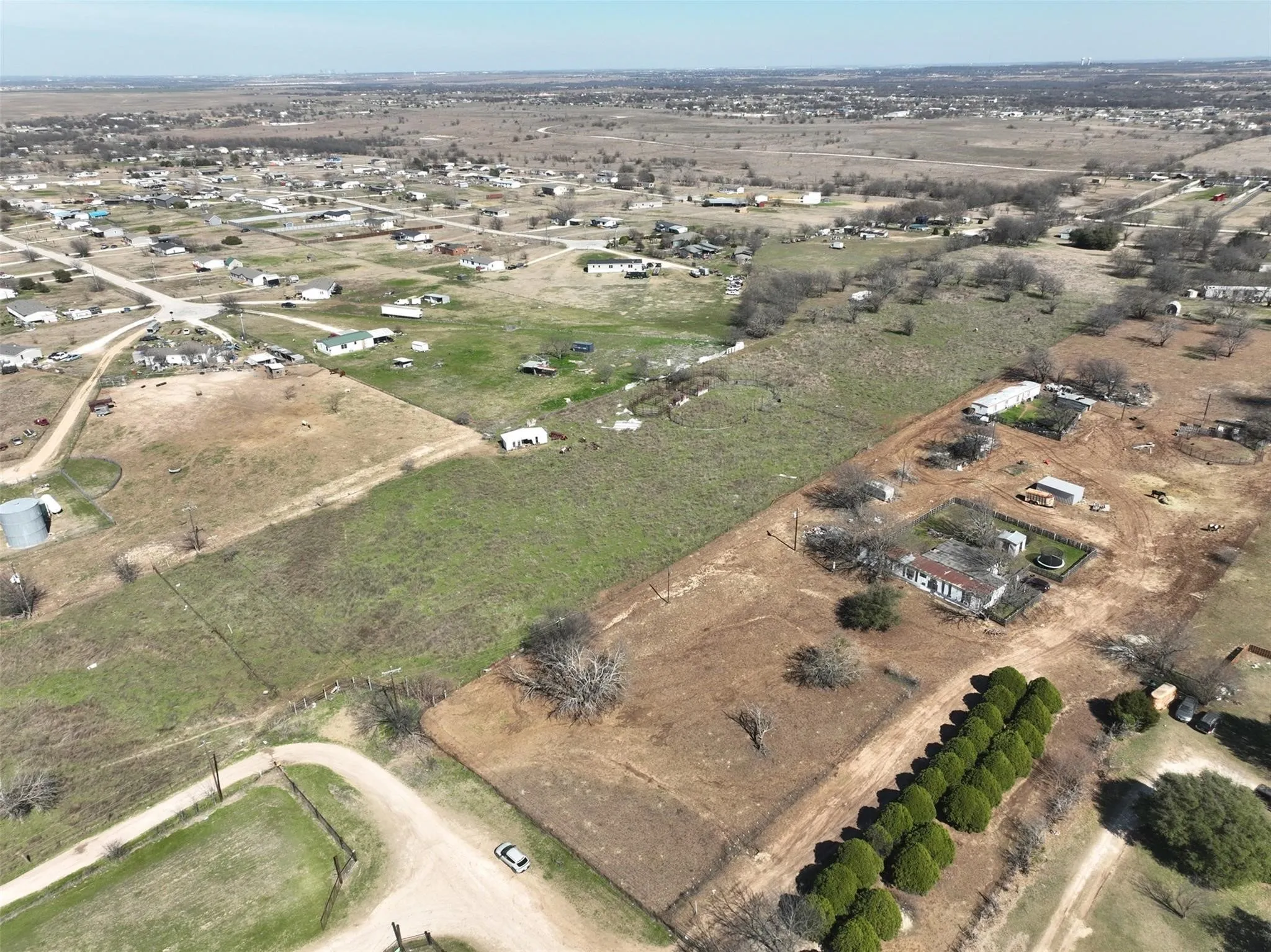 Expansive rural property featuring a residential structure, multiple outbuildings, mature trees, and open land