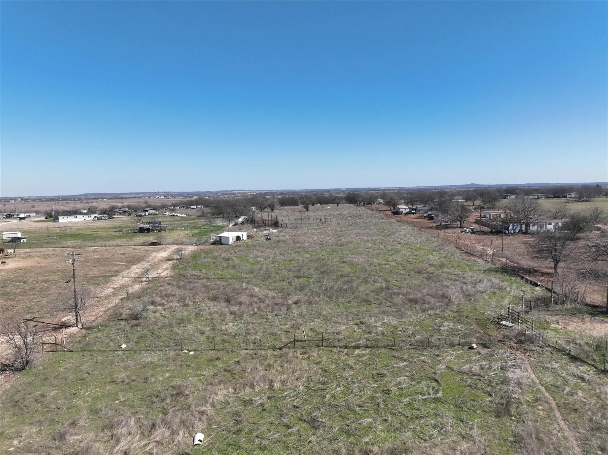 Expansive undeveloped land featuring a clear blue sky, distant structures, and open fields