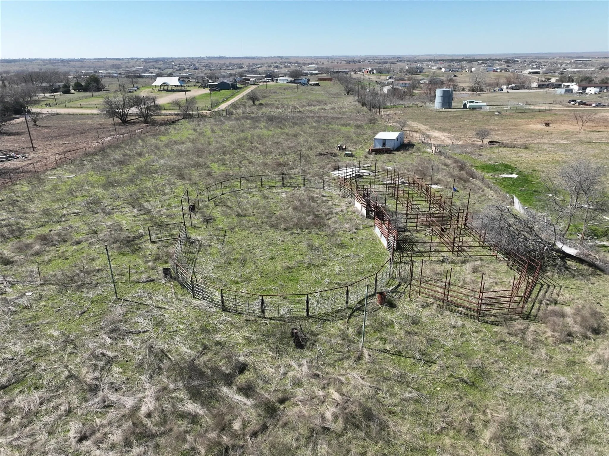 Expansive land featuring a circular metal pen, additional metal fencing, and a small white outbuilding