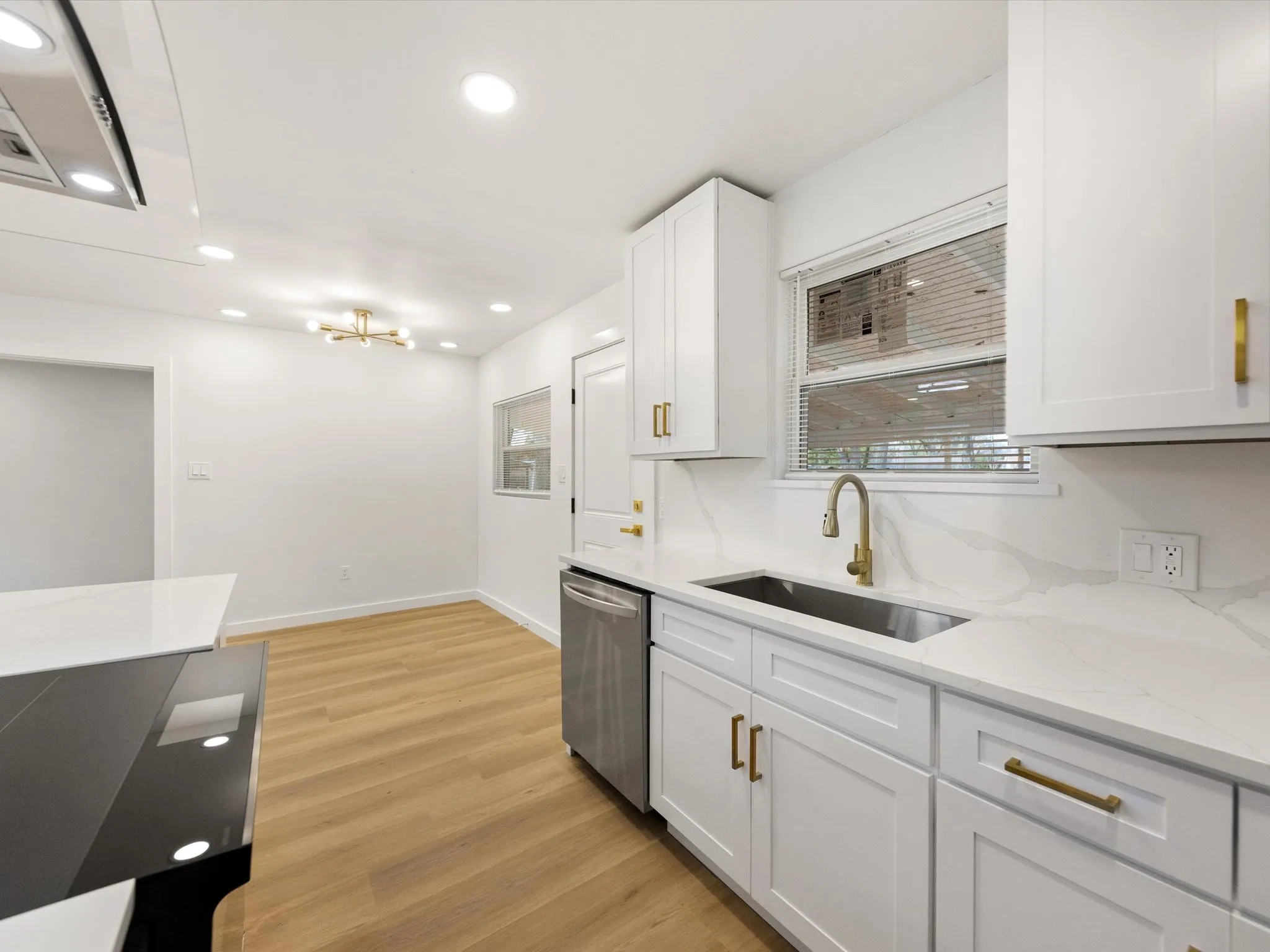 White shaker cabinetry with gold-finish hardware, stainless steel sink, wood-finish flooring, recessed lighting, and a built-in cooktop