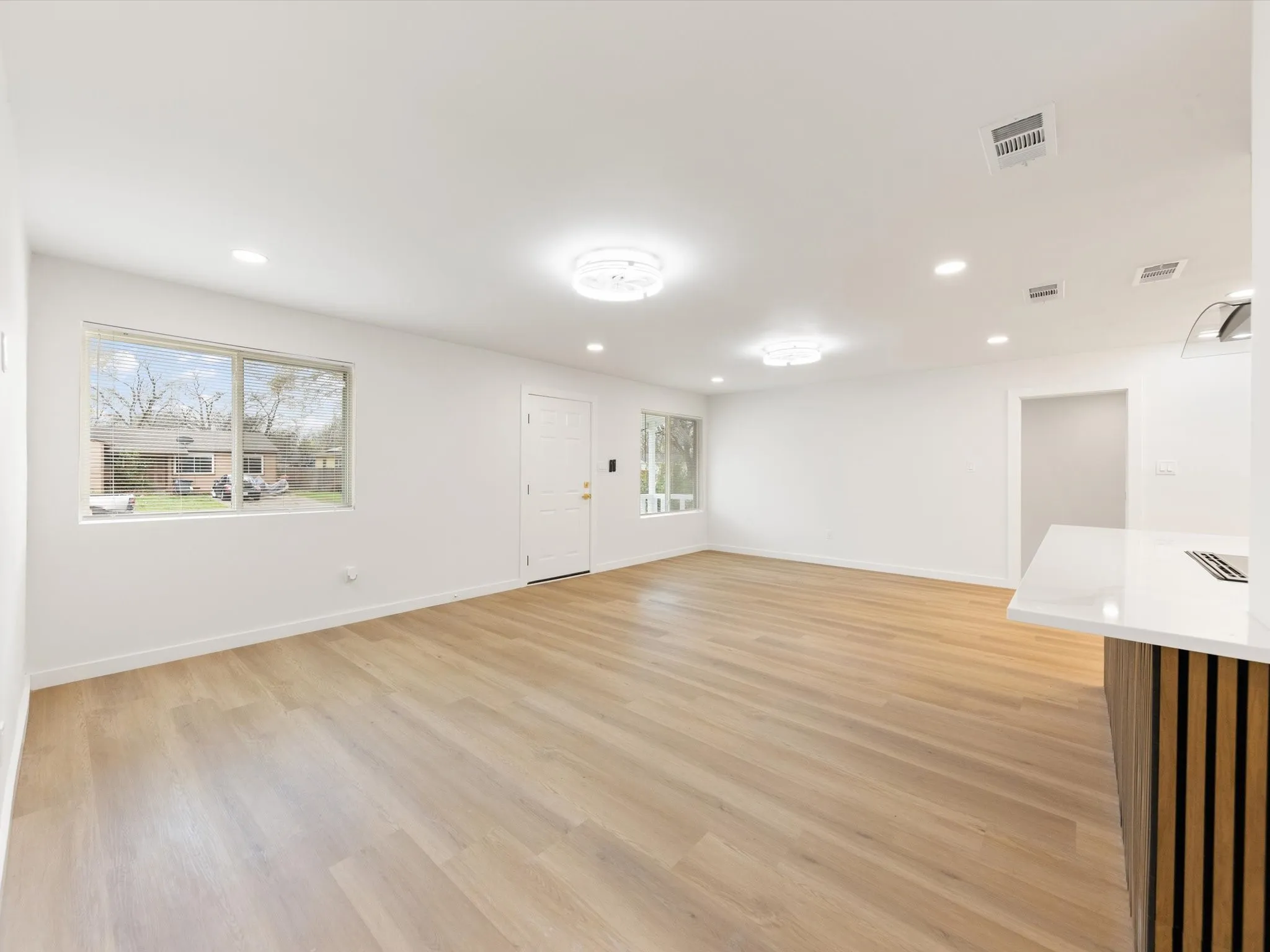 Light wood-finish flooring with recessed lighting and two ceiling-mounted light fixtures