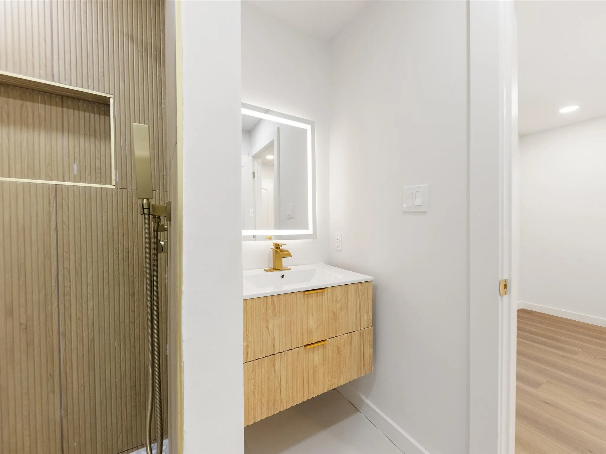 Modern bathroom featuring a wood-finish floating vanity with an integrated white countertop and single basin sink, paired with a brass-finish faucet