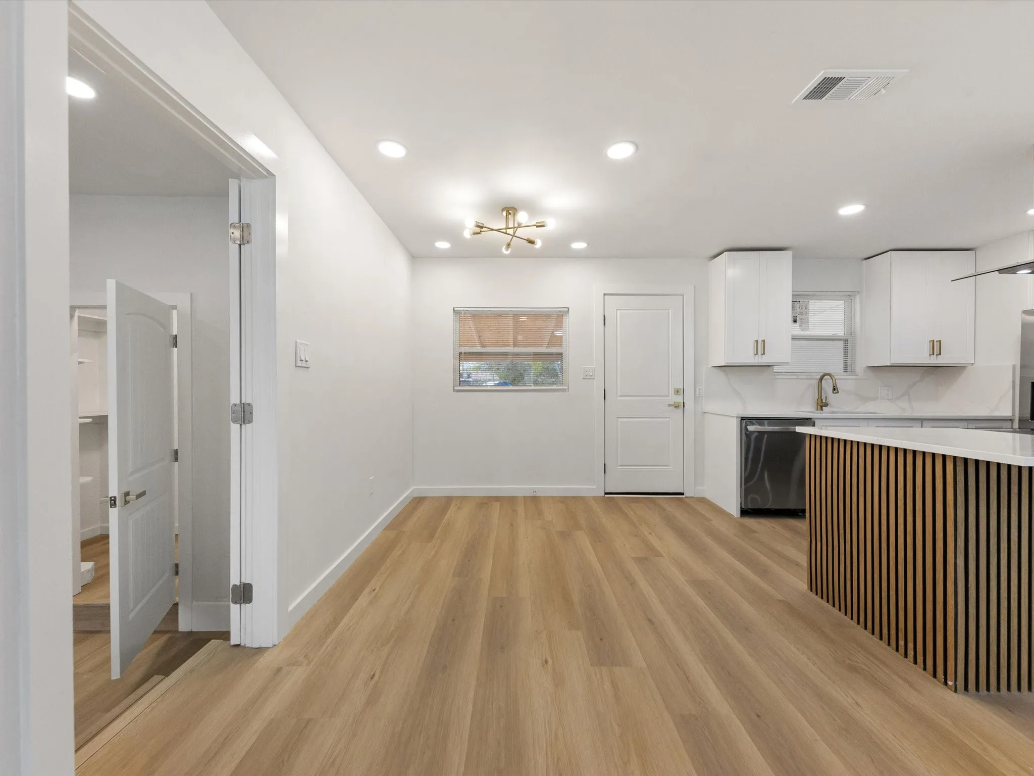 Wood-finish flooring, recessed lighting, white cabinetry, a kitchen island with a slatted wood-finish base, and a stainless steel dishwasher