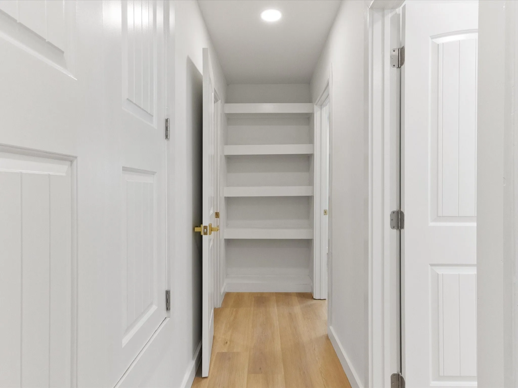 Hallway featuring wood-finish flooring, white paneled doors, recessed lighting, and built-in shelving