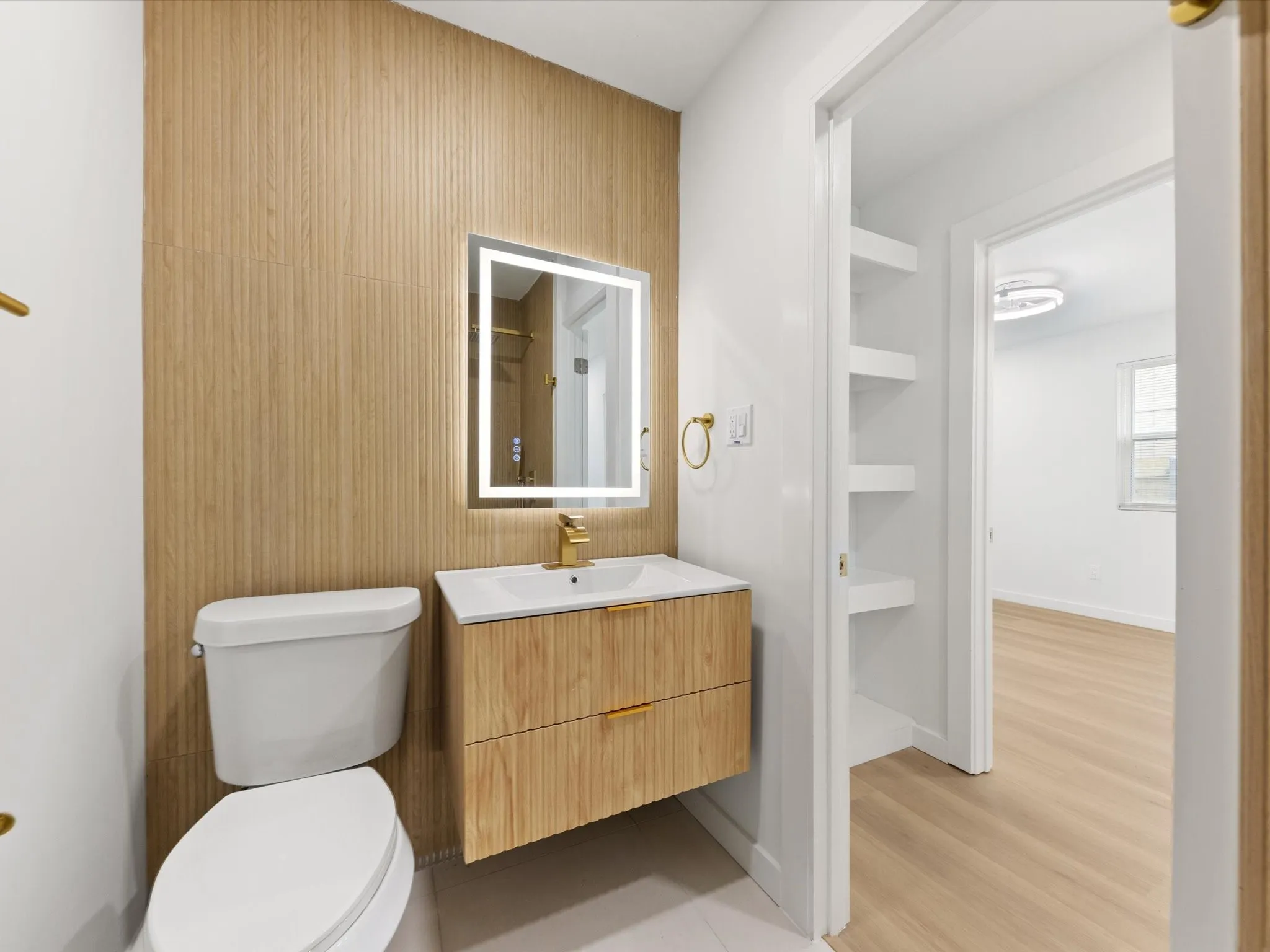 Bathroom featuring a floating vanity with a vessel sink, an illuminated mirror, and a wood-finish accent wall