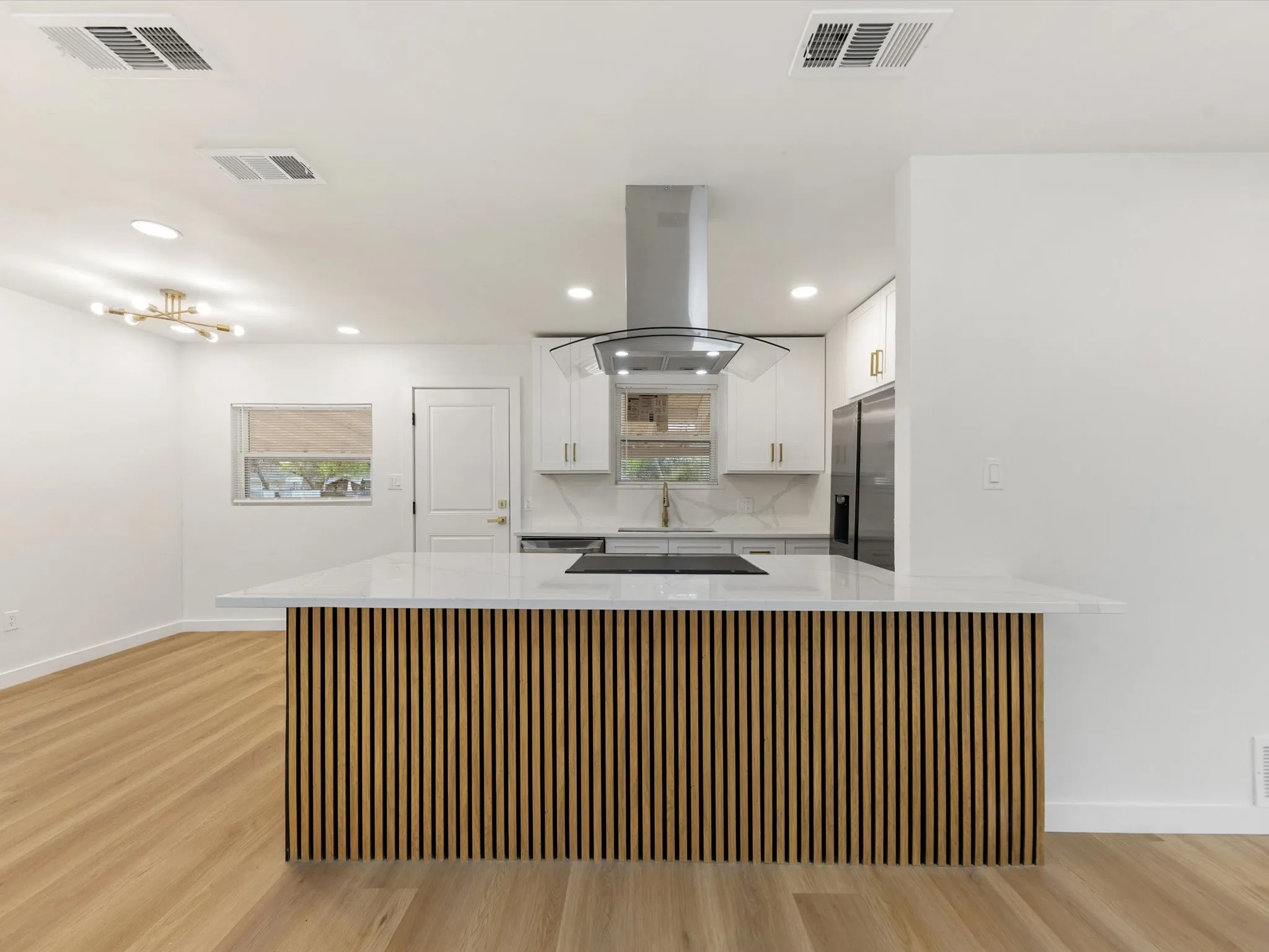Open-concept kitchen featuring a waterfall island with slatted wood paneling, white cabinetry, integrated range hood, and stainless steel appliances