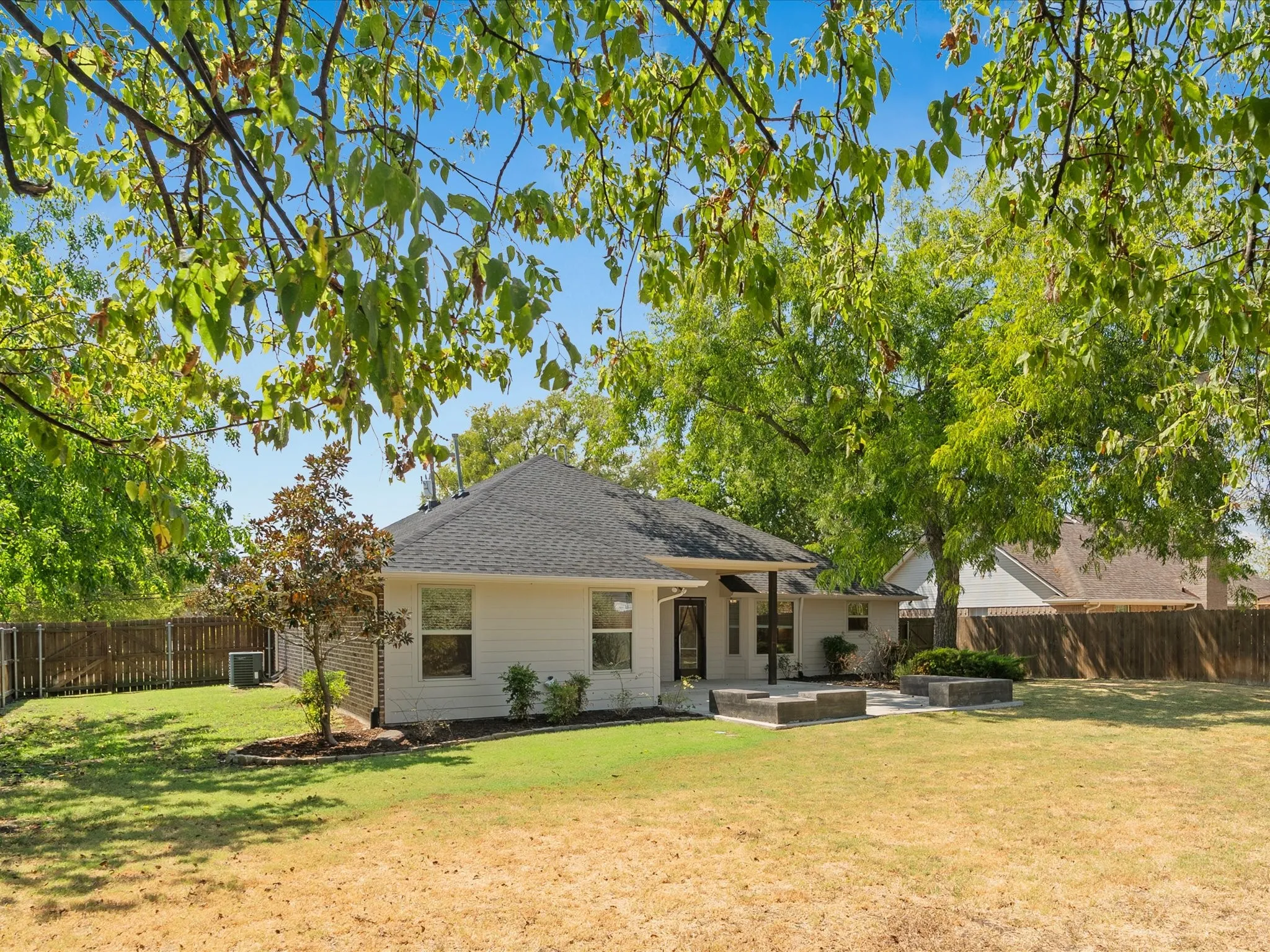 Expansive backyard featuring a partial privacy fence, concrete patio, and mature trees