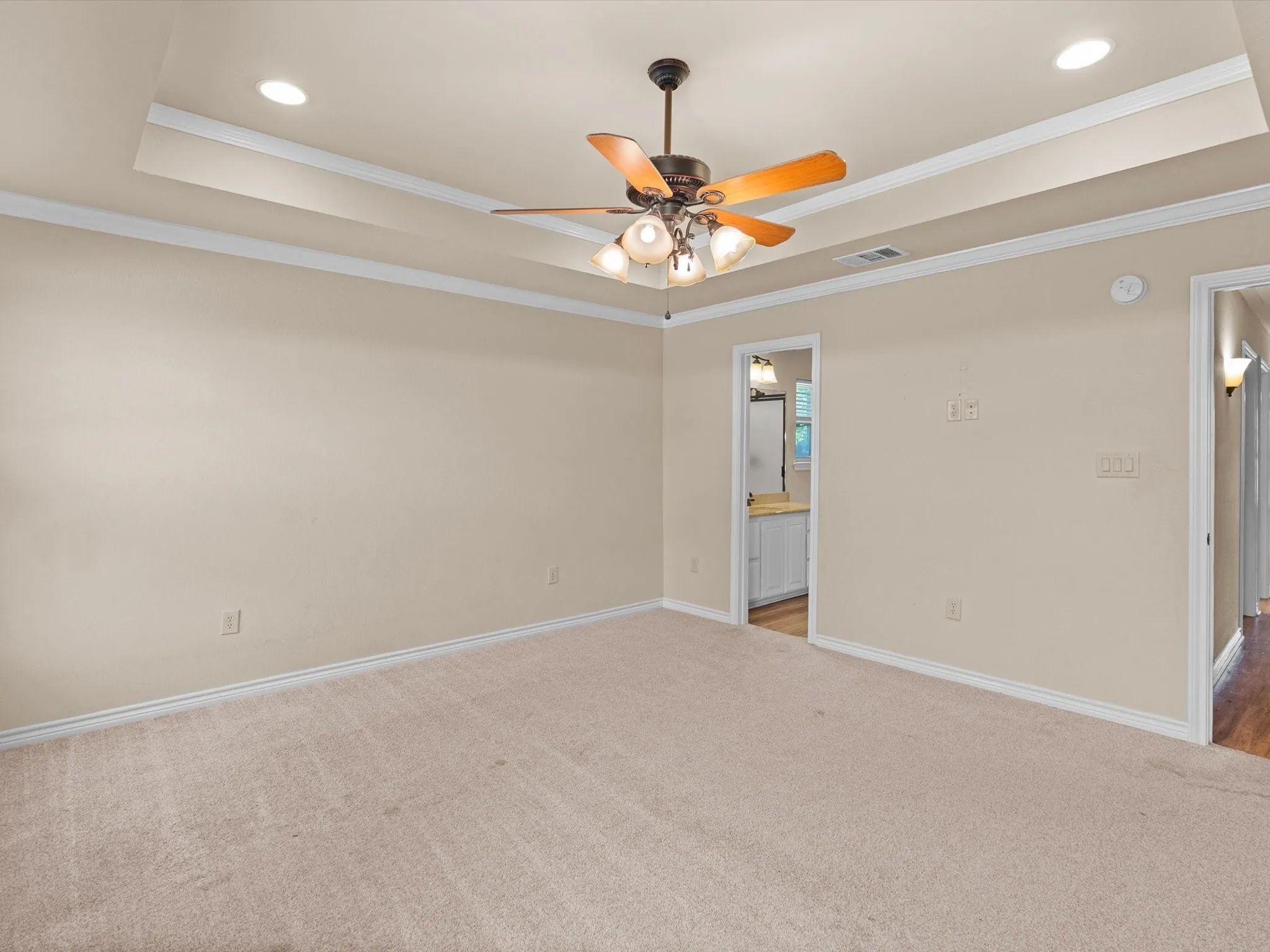 Recessed lighting, tray ceiling, ceiling fan with integrated lighting, neutral carpet flooring, and an open doorway