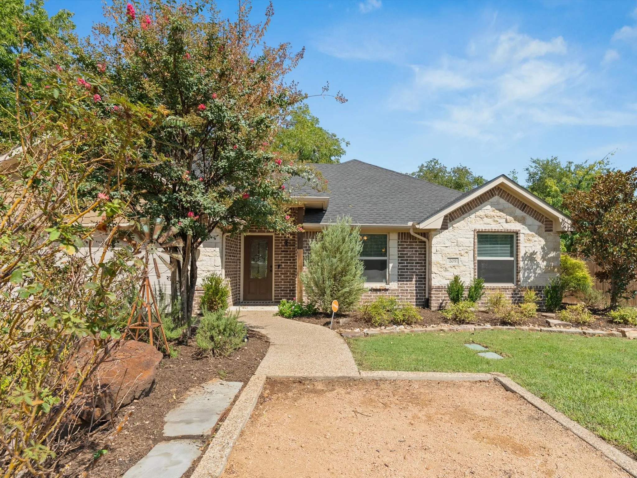 Brick and stone exterior with a gabled roofline, mature landscaping, and a concrete pathway