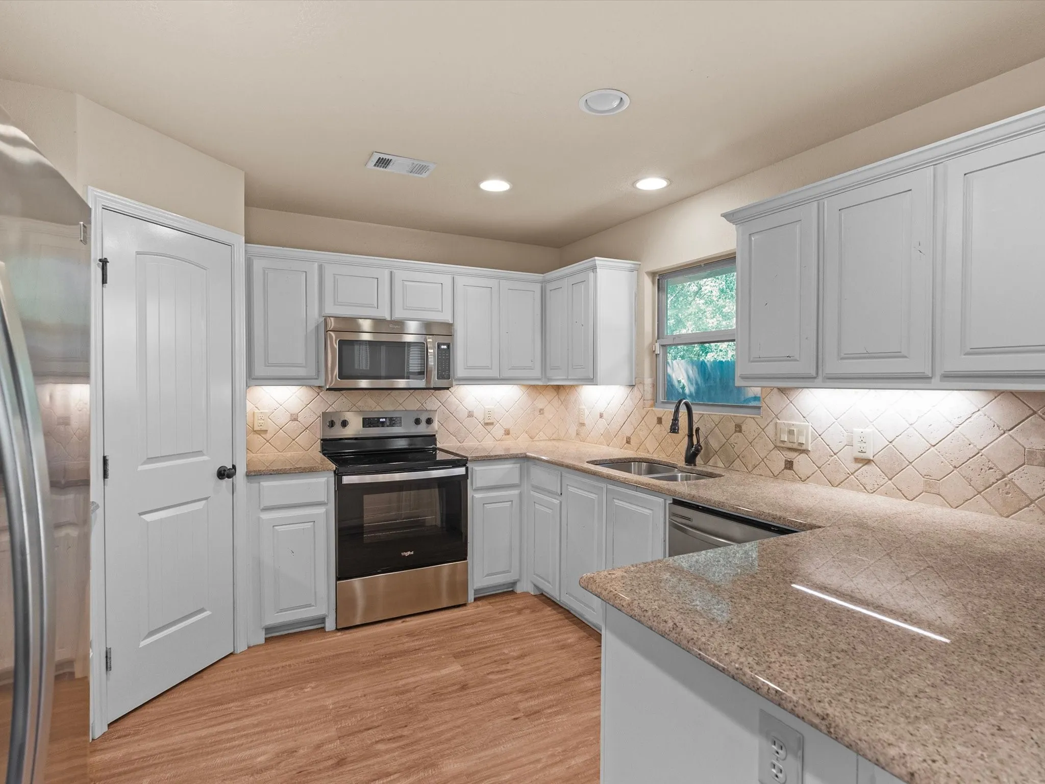 Kitchen featuring wood-finish flooring, light-toned cabinetry, stainless steel appliances, and a tiled backsplash