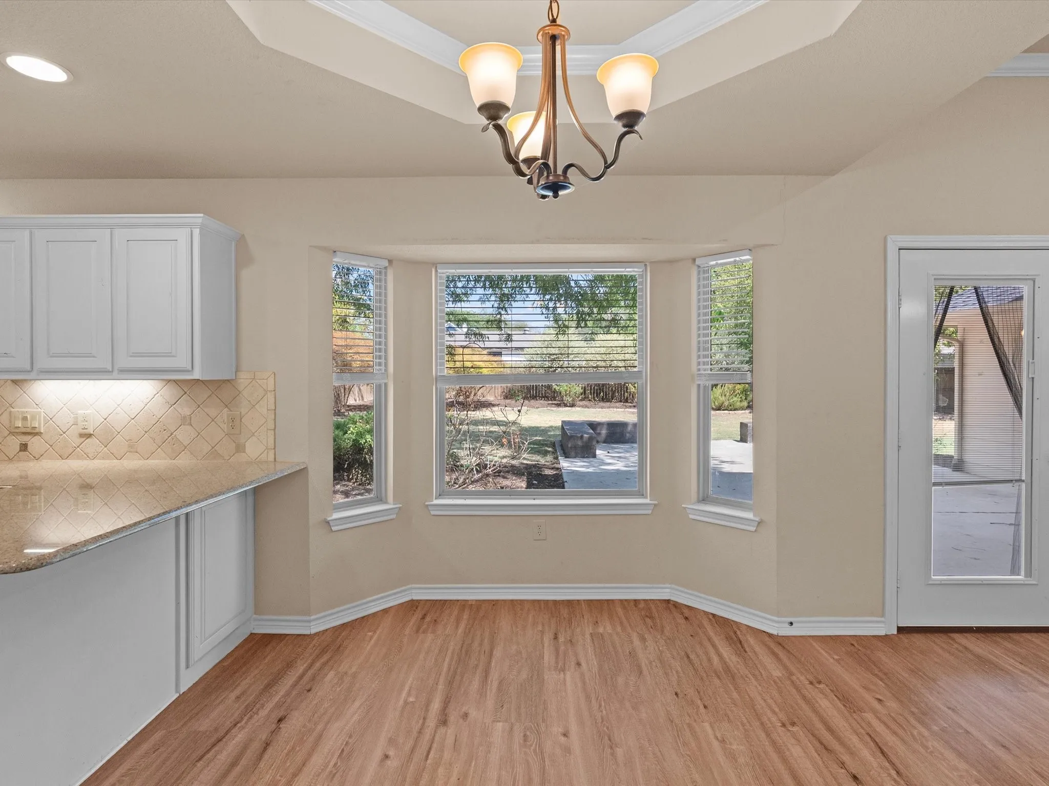 Wood-finish flooring with a bay window, white cabinetry, and a full-light door