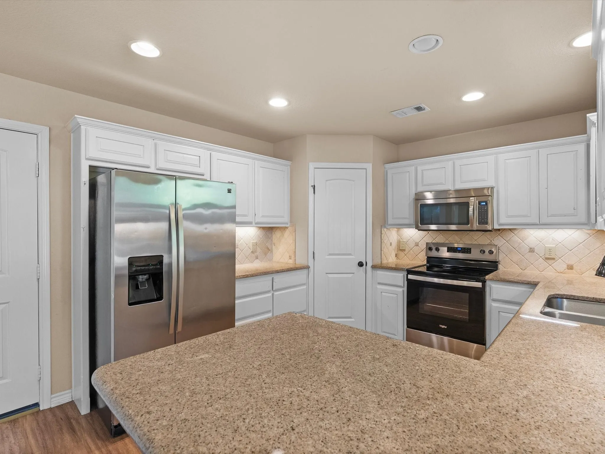 Kitchen featuring white cabinetry, stainless steel appliances, speckled countertops, tile backsplash, and recessed lighting