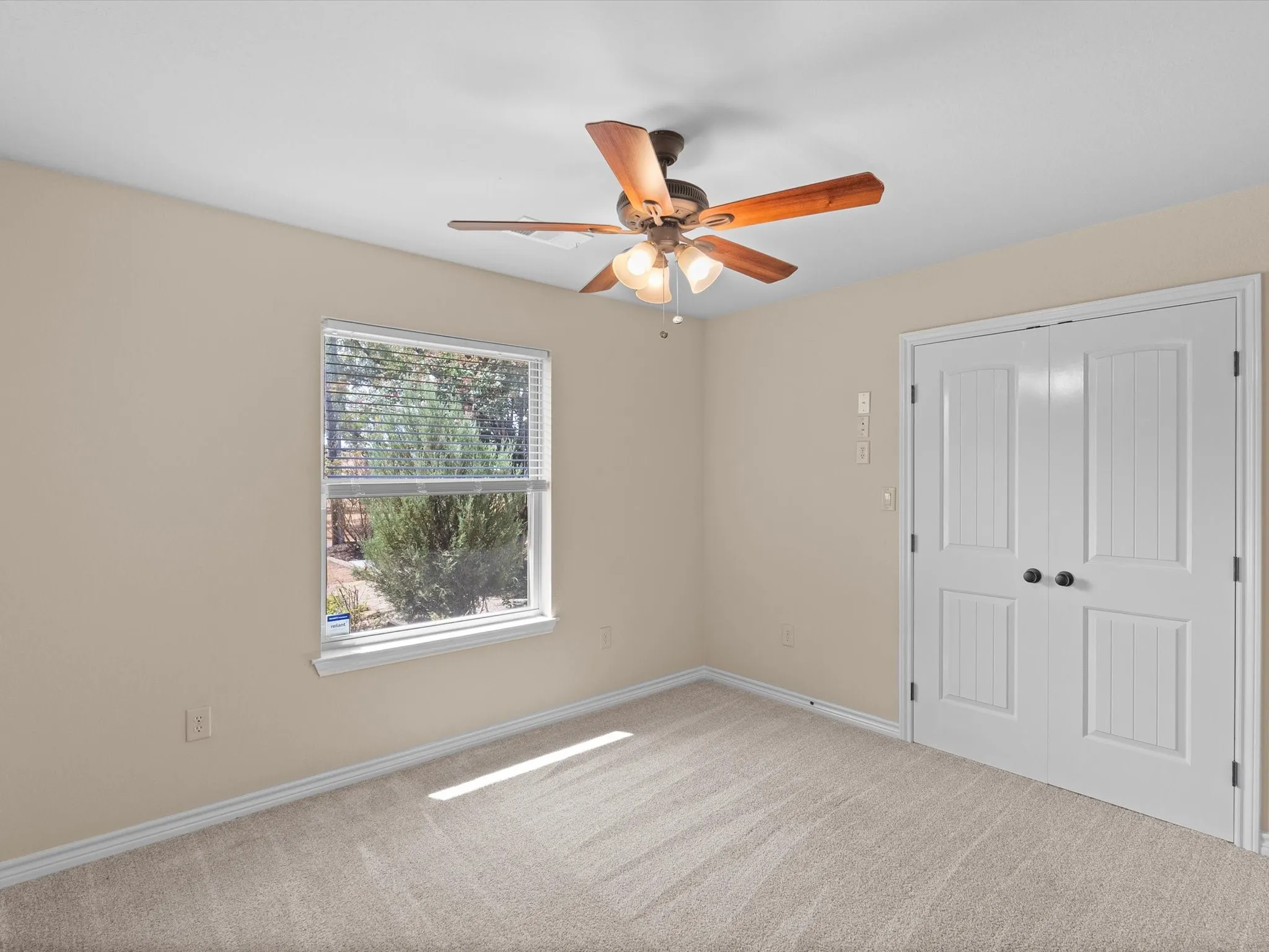 Neutral-toned walls, plush carpeting, a ceiling fan with integrated lighting, a window with horizontal blinds, and paneled double doors