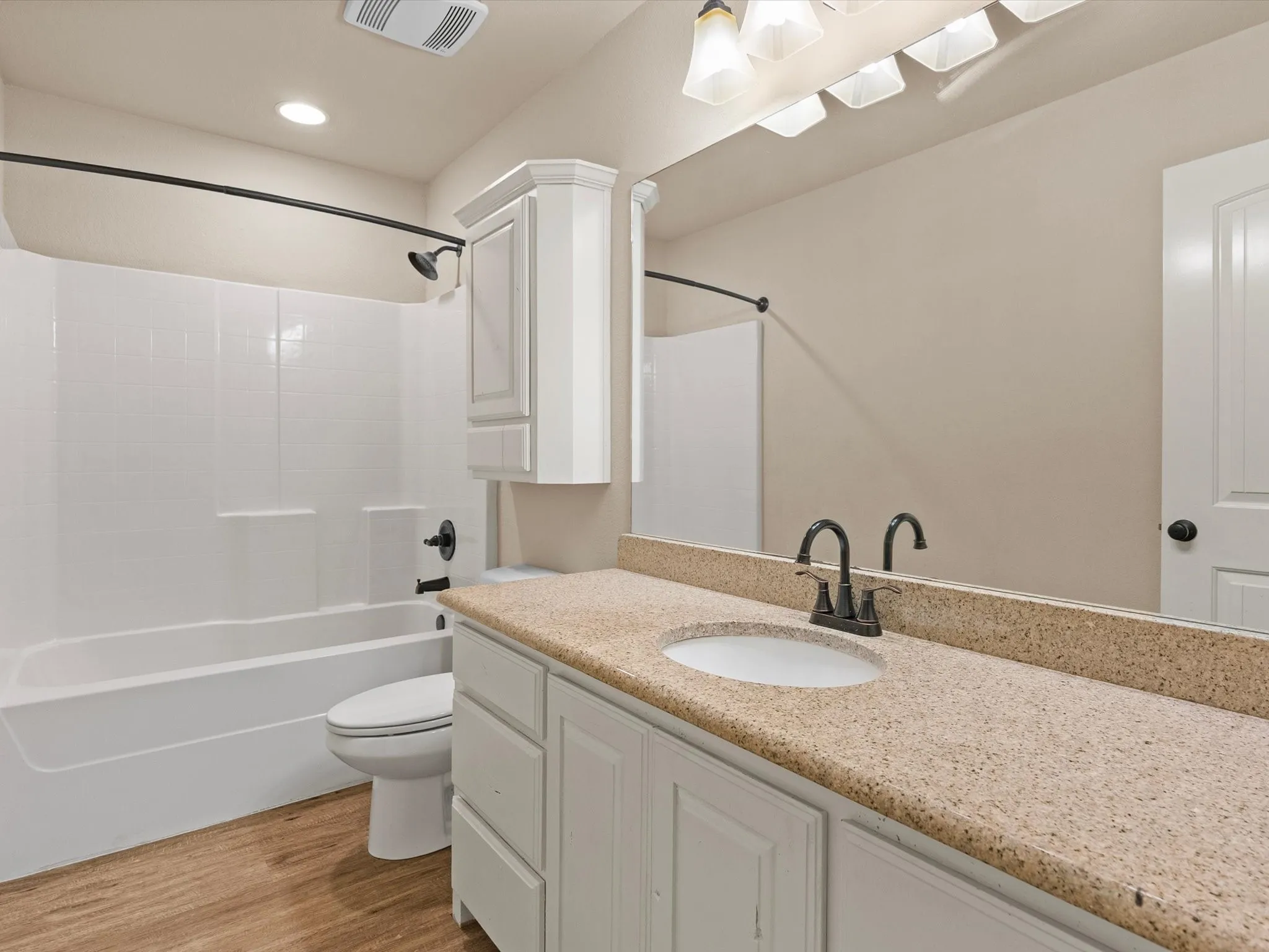 Bathroom featuring a single vanity with a light-colored countertop, an undermount sink, a white bathtub with a shower, and wood-finish flooring