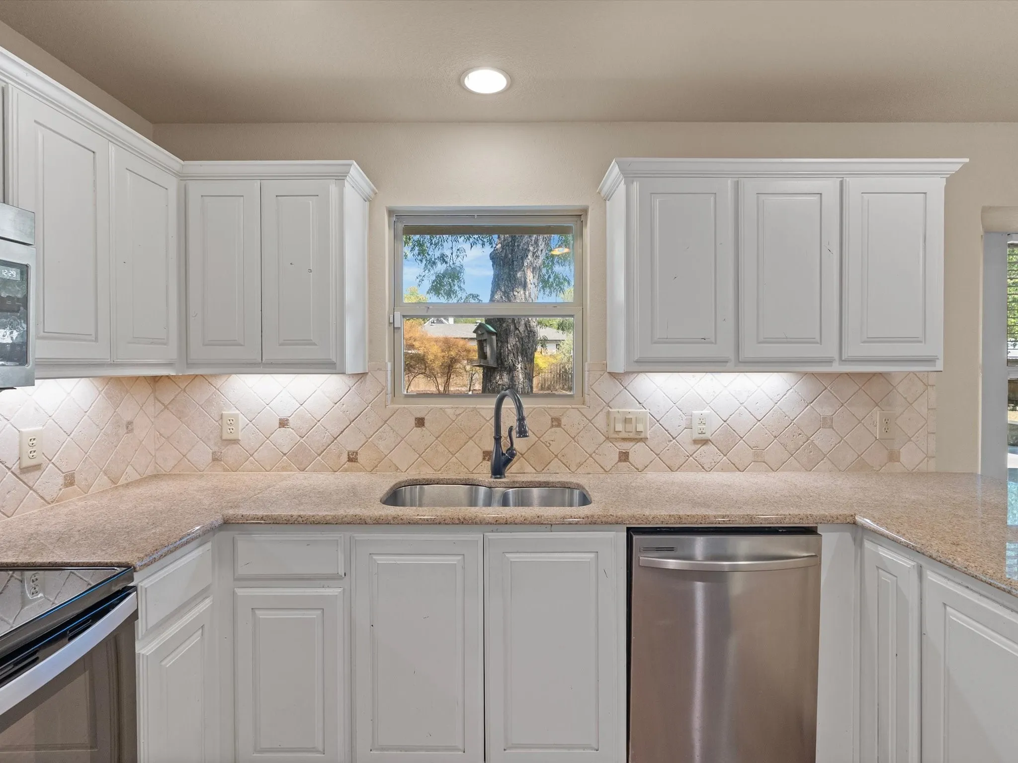 White cabinetry with crown molding, undermount sink, stainless steel dishwasher, tile backsplash, and recessed lighting
