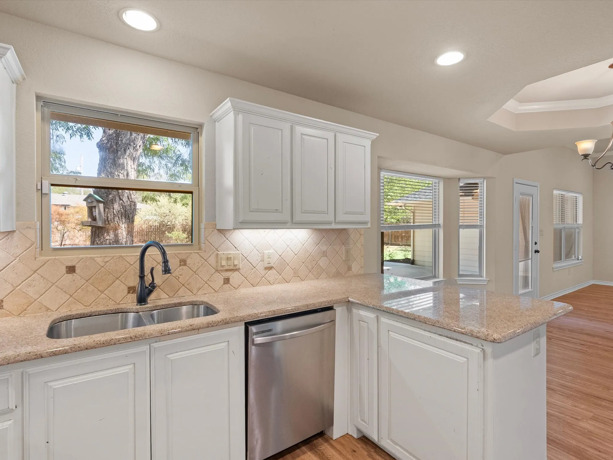 Kitchen featuring a double basin stainless steel sink, a stainless steel dishwasher, white cabinetry, solid surface countertops, and a tile backsplash