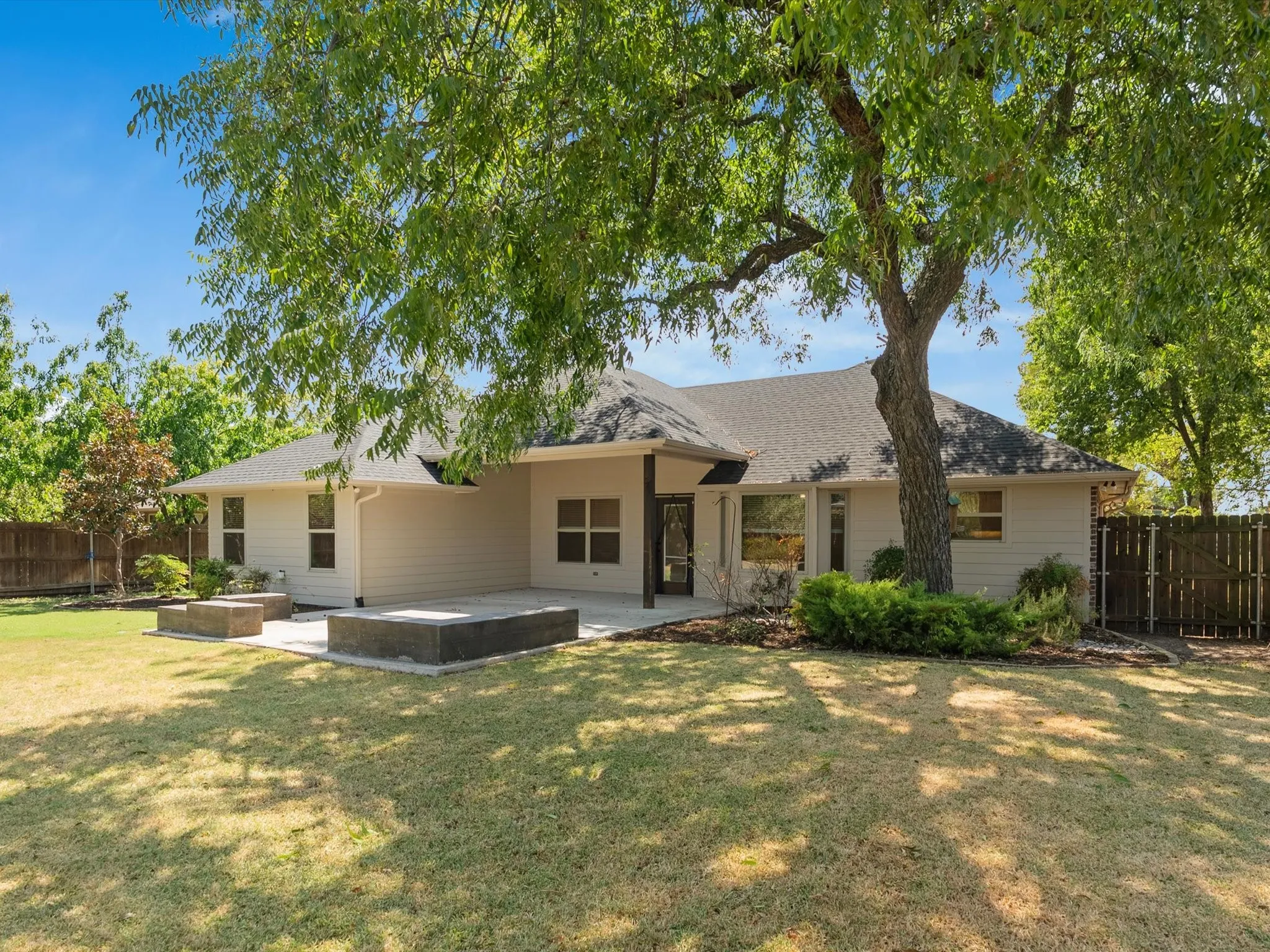 Expansive backyard featuring a large tree, concrete patio, and two built-in raised planters