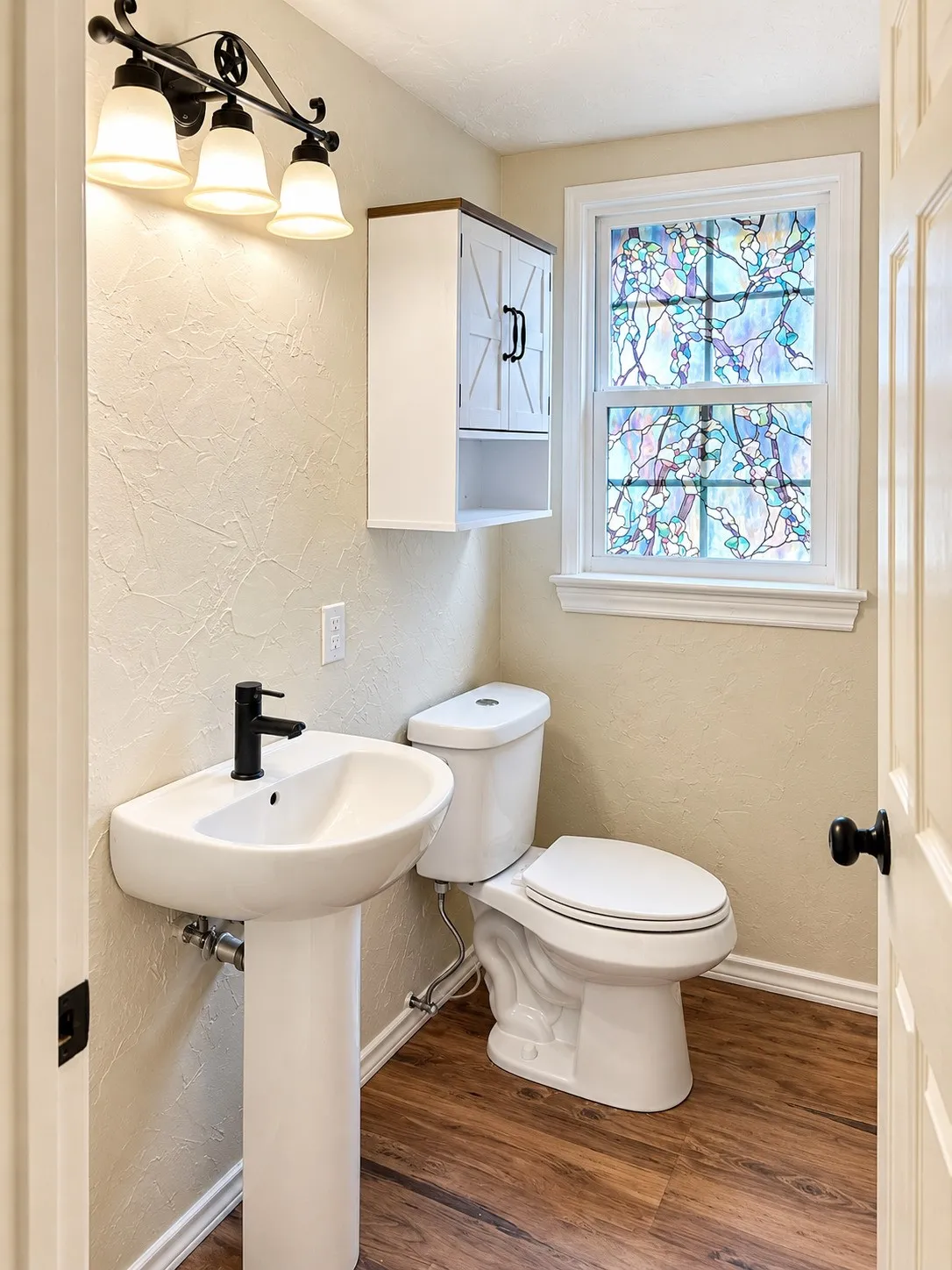 Pedestal sink with a matte black faucet, wall-mounted storage cabinet, and wood-finish flooring