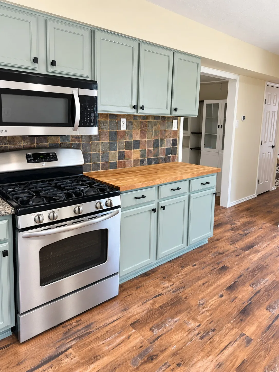 Stainless steel range, stainless steel microwave, wood-finish flooring, and light-toned cabinetry with dark hardware
