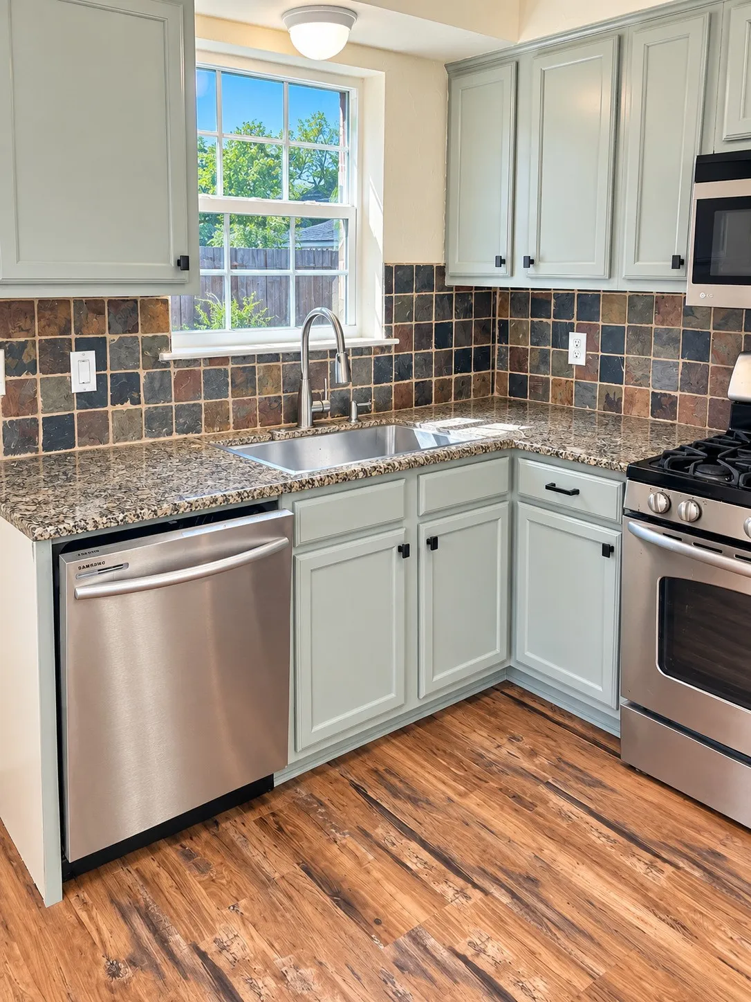 Light-toned cabinetry with dark hardware, stone tile backsplash, granite-finish countertops, stainless steel appliances, and wood-finish flooring