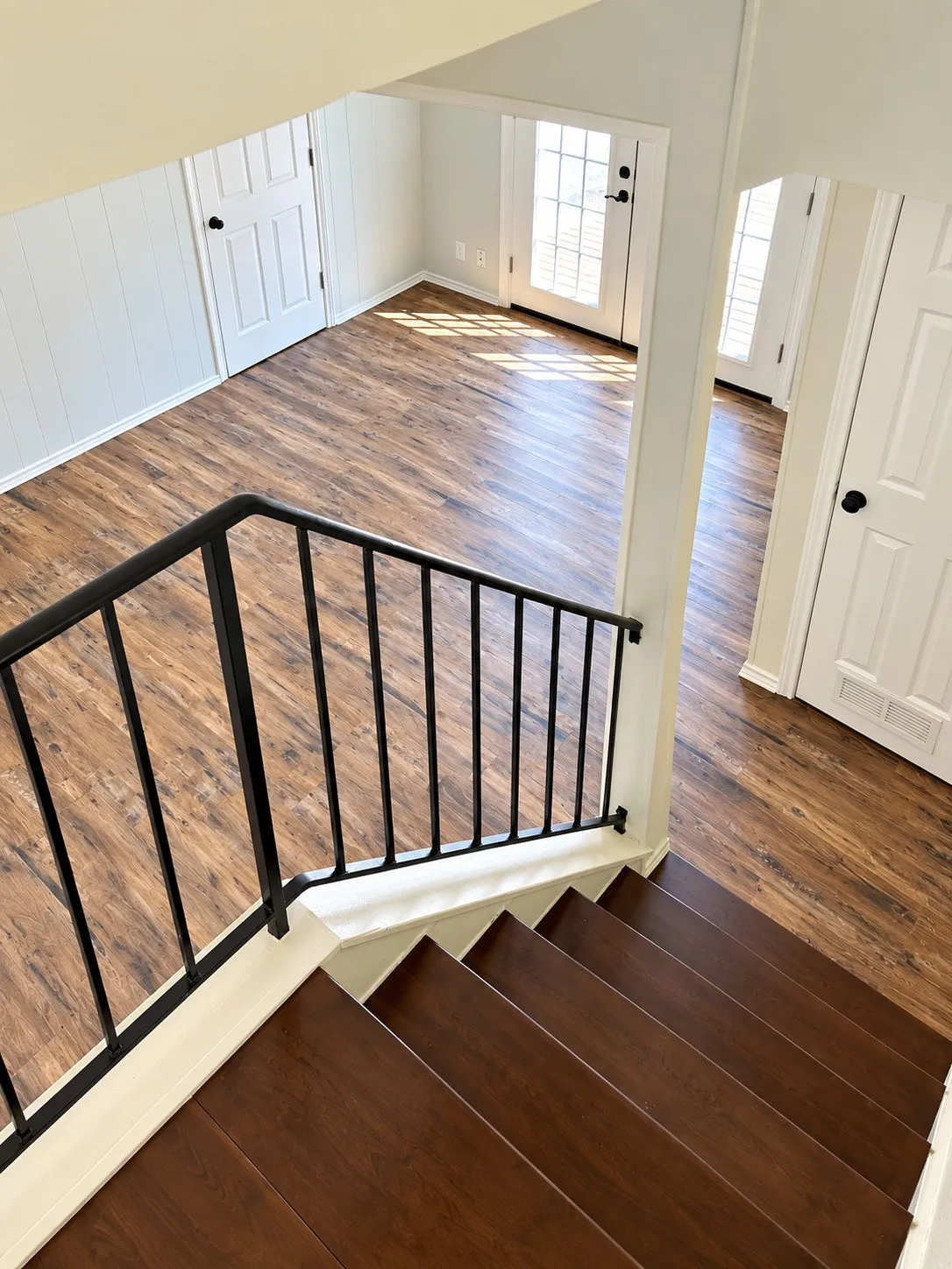Hardwood stairs with wrought iron railing, wood-finish flooring, white paneling, and French doors