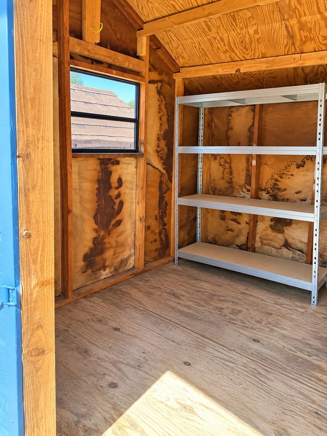 Wood-paneled interior walls, wood-finish flooring, single-pane window, and a built-in shelving unit