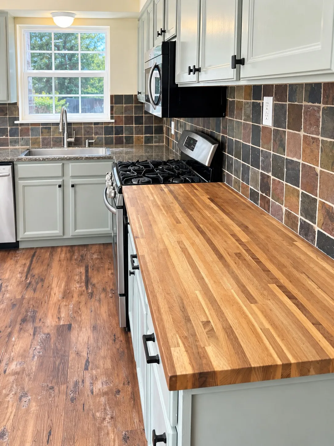 Butcher block countertops, wood-finish flooring, stainless steel appliances, shaker-style cabinetry, and a tile backsplash