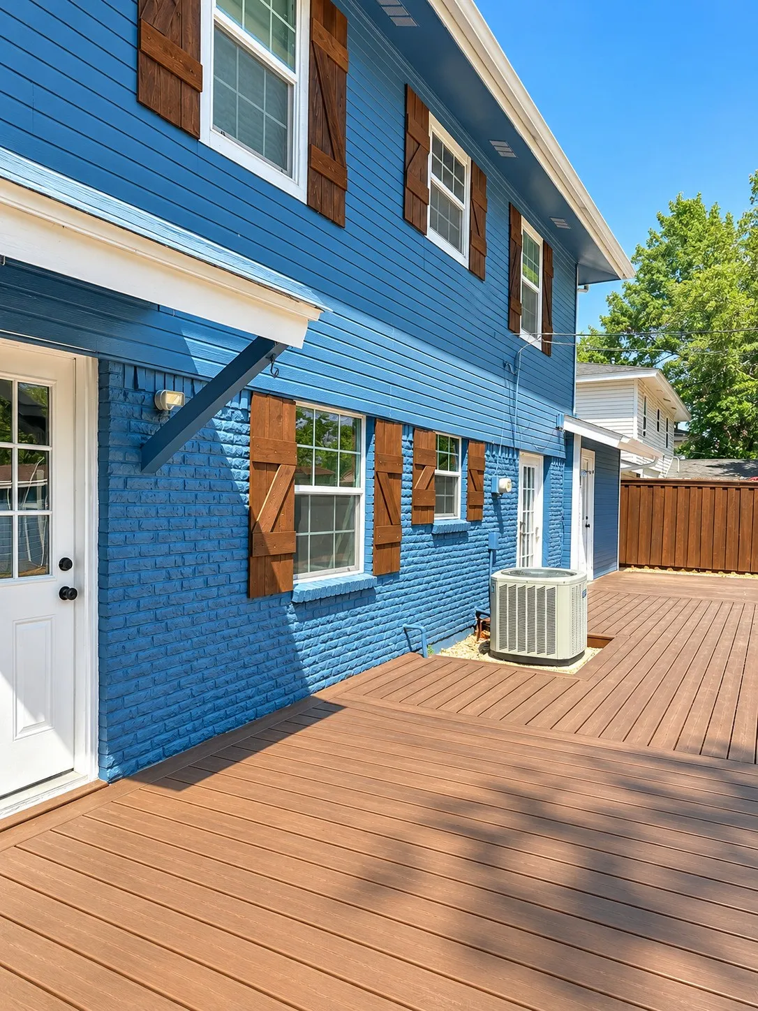 Expansive outdoor decking, blue brick and siding exterior, white-framed windows with wood shutters, and a white entry door
