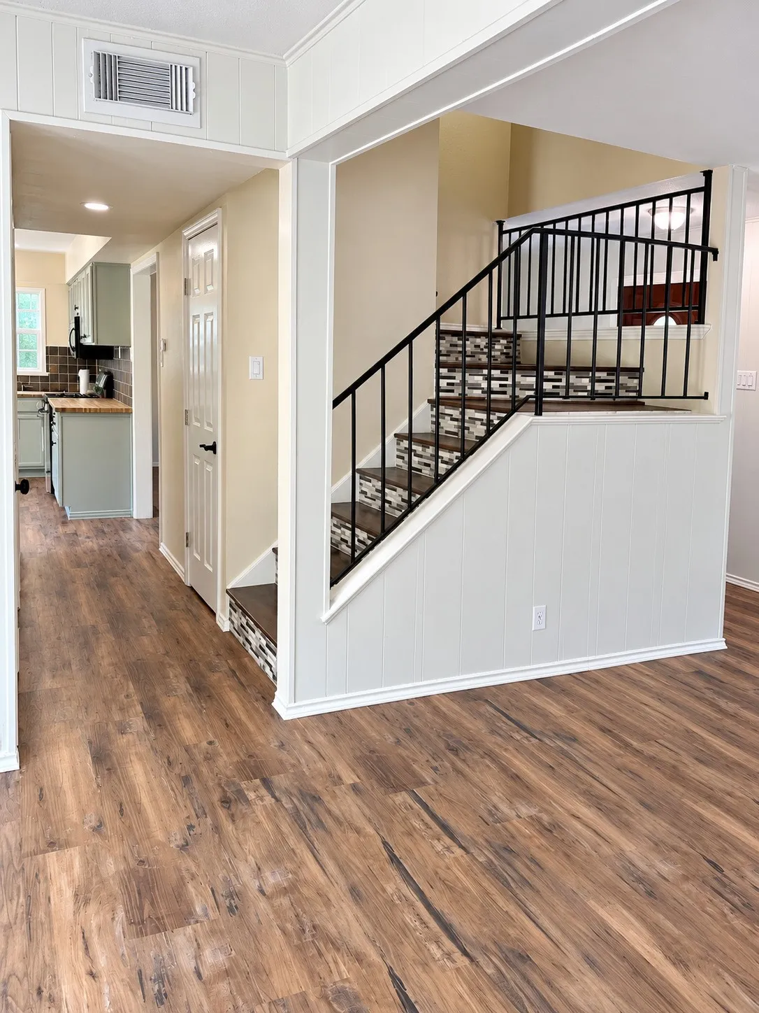 Wood-finish flooring throughout, staircase with decorative tile risers and wrought iron railing, and beadboard paneling