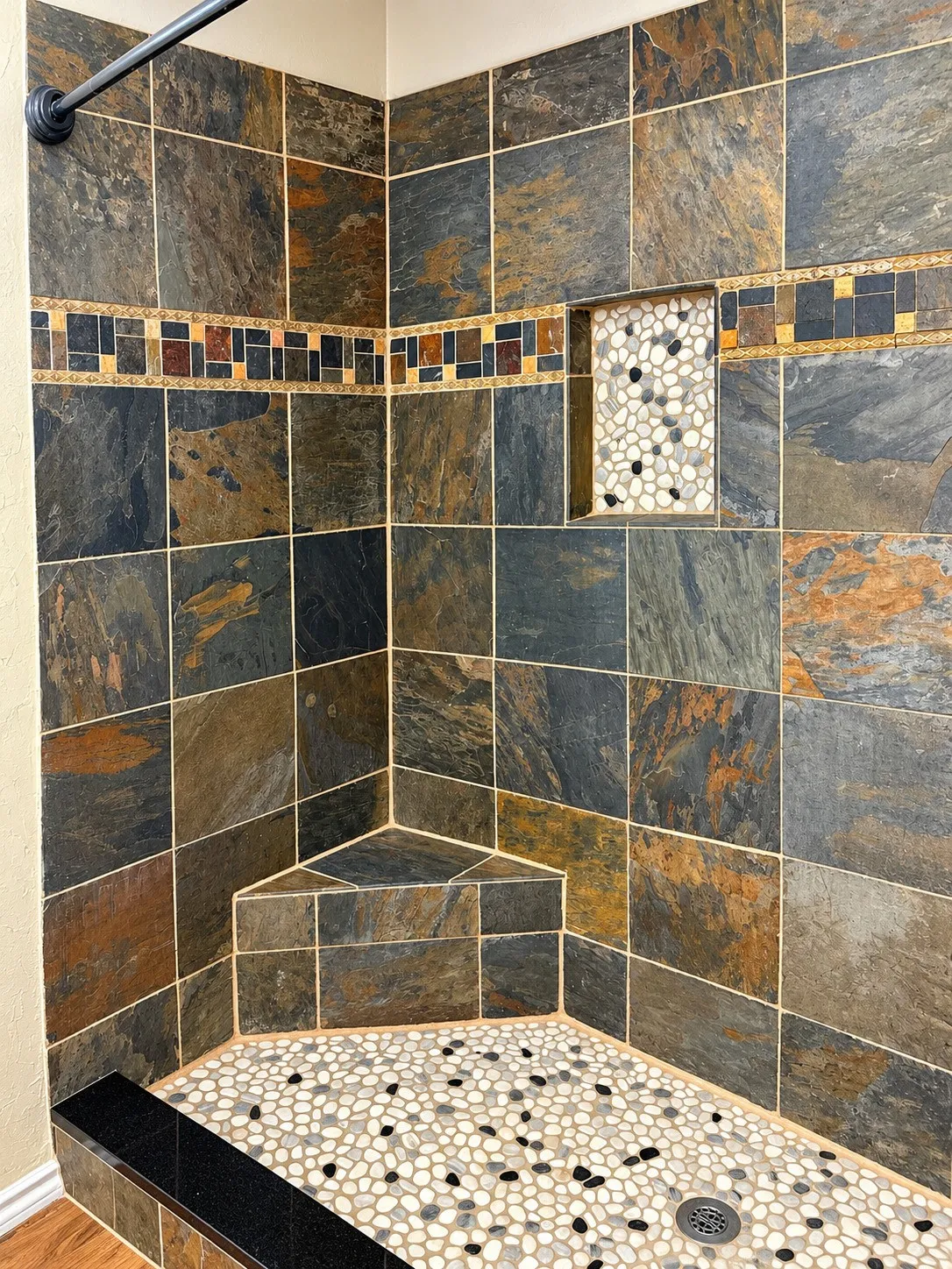 Tiled shower enclosure featuring a corner bench, integrated niche with pebble tile, and a decorative mosaic border