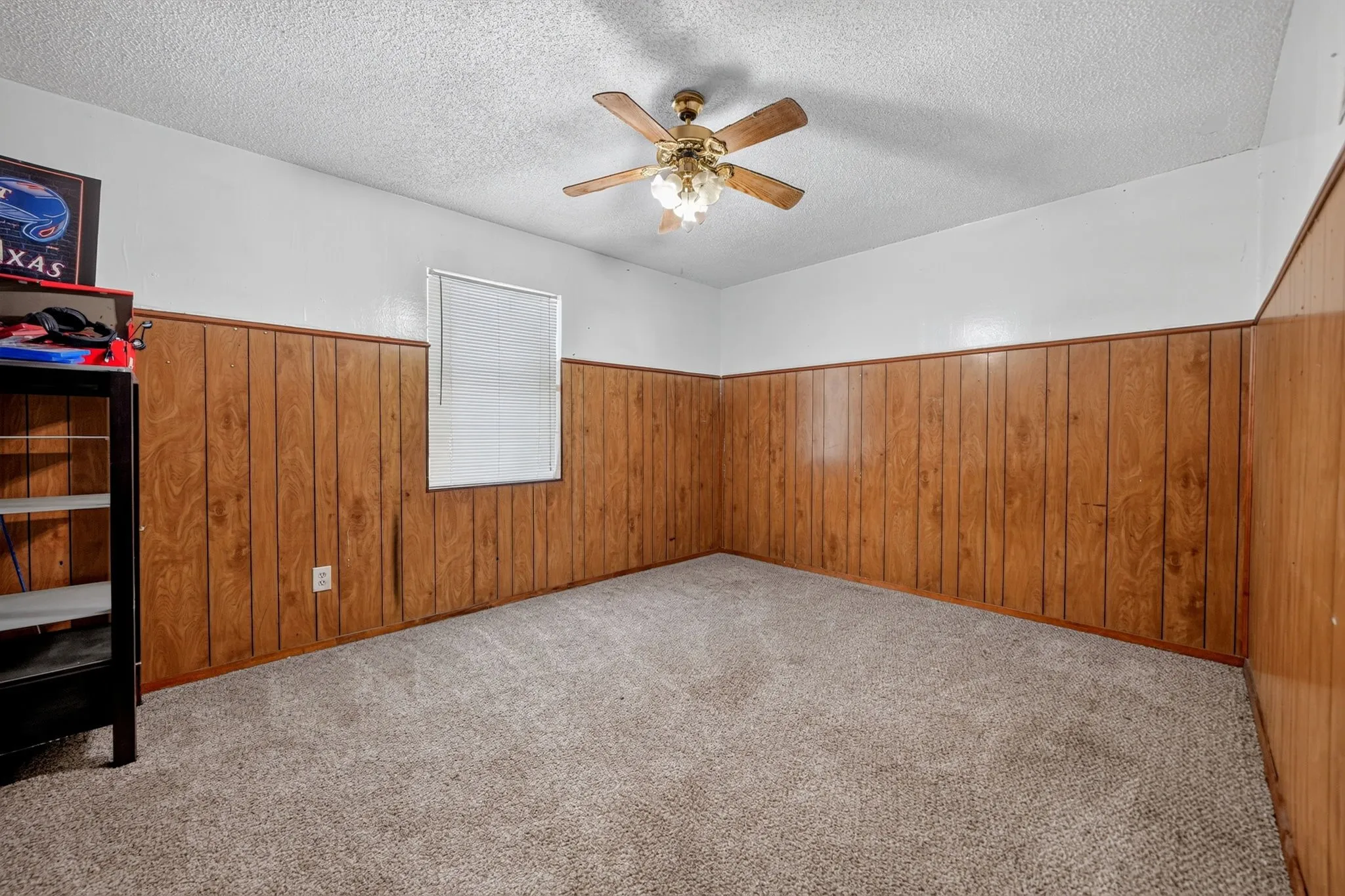 Carpeted room featuring wood paneling, white painted walls, and a ceiling fan with integrated lighting