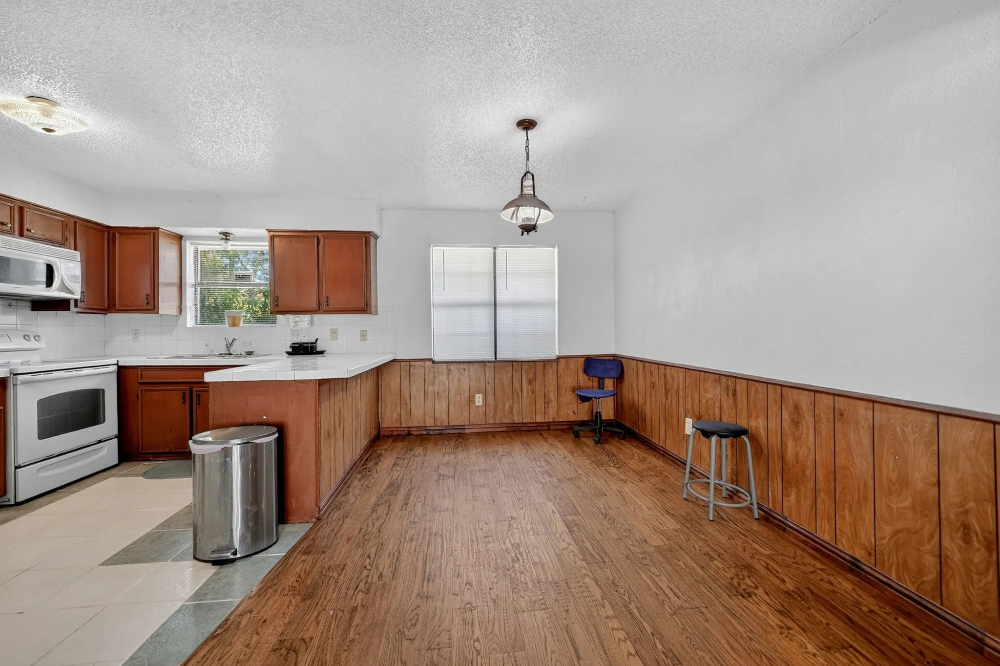 Wood-finish flooring, wood paneling, white walls, and a white ceiling with a single pendant light fixture