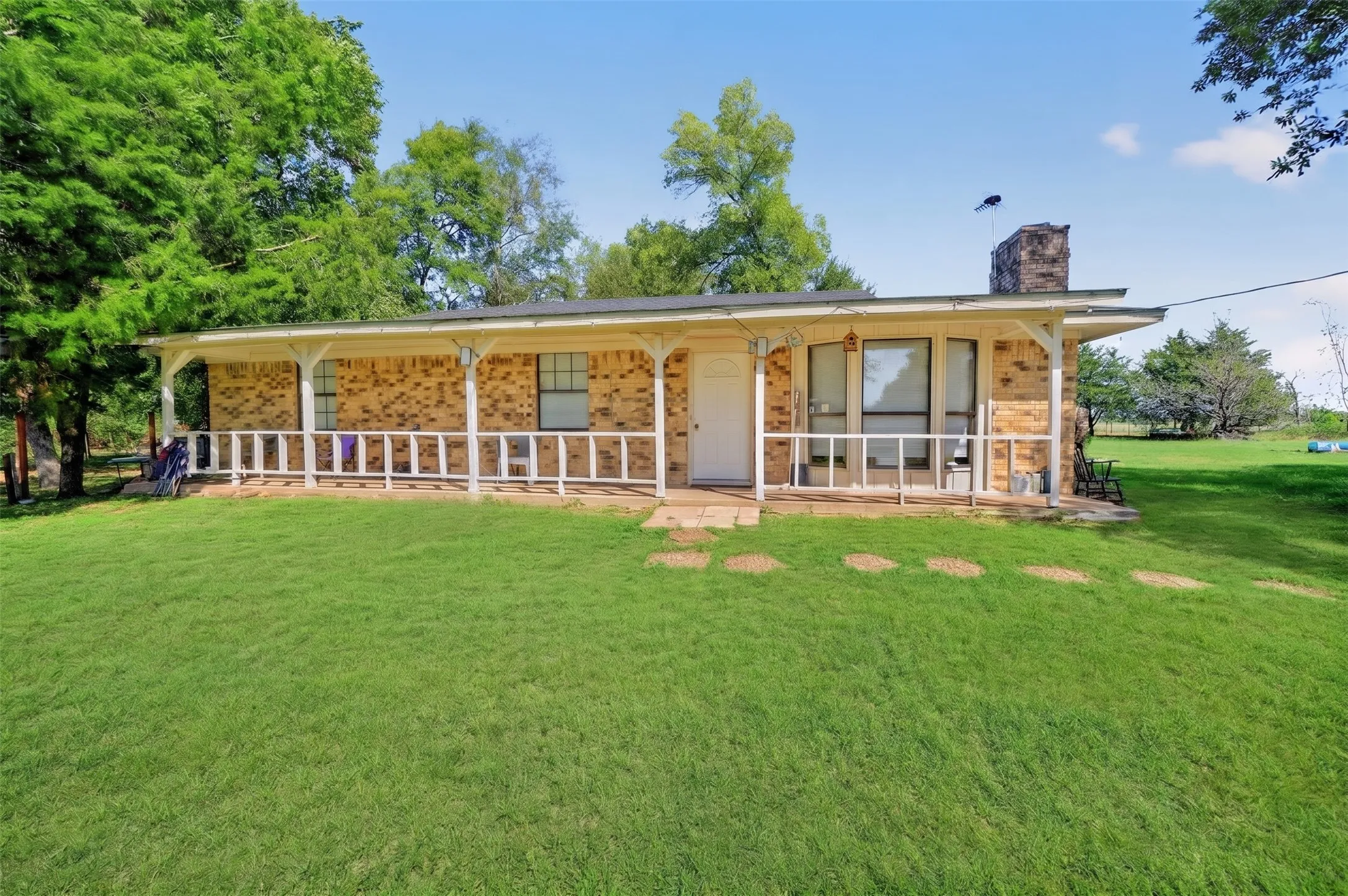 Brick exterior with a covered front porch and white railings, featuring a stone chimney and expansive green lawn