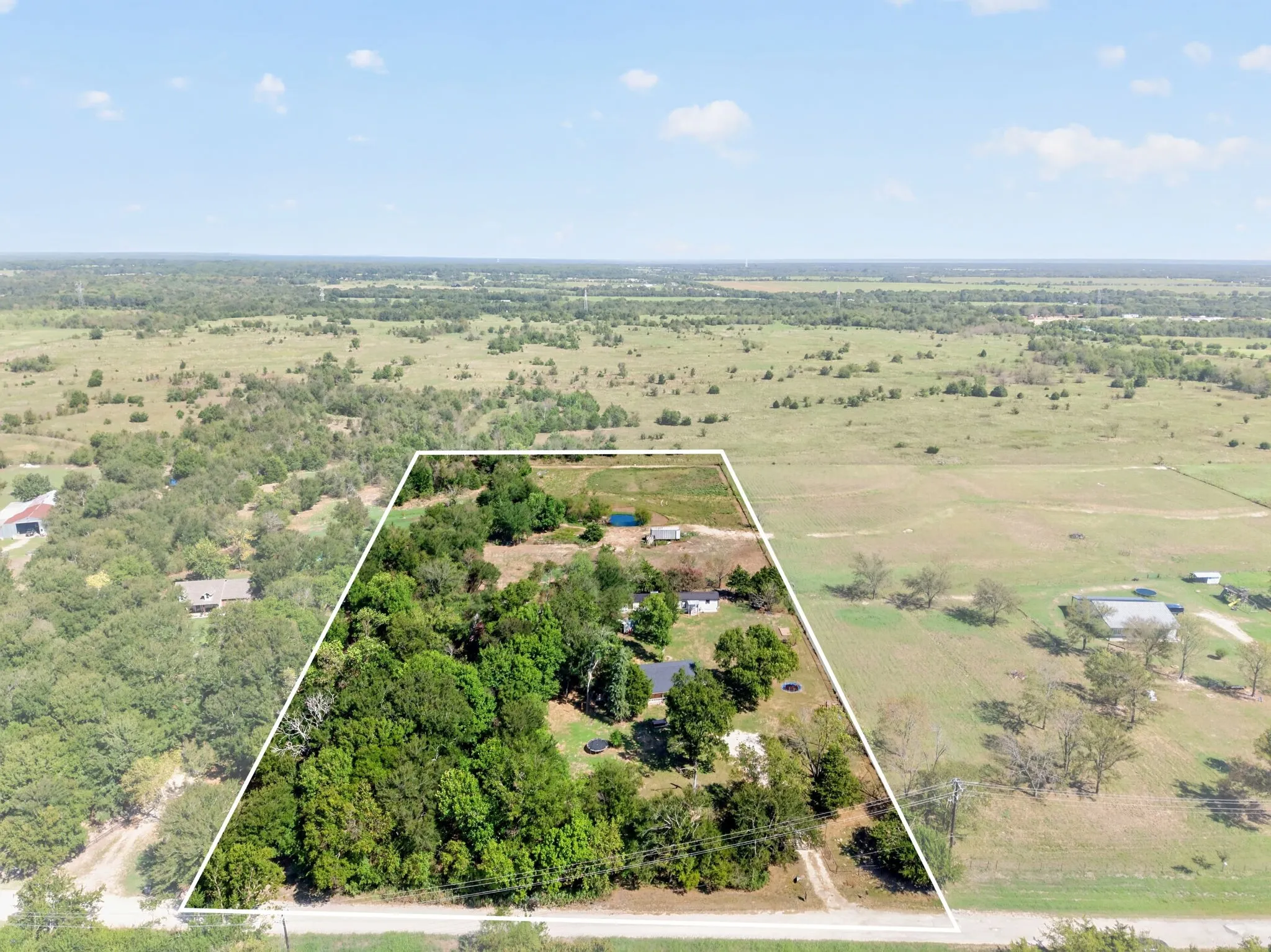 Expansive acreage featuring mature trees, open land, a private pond, and a residence with a dark roof