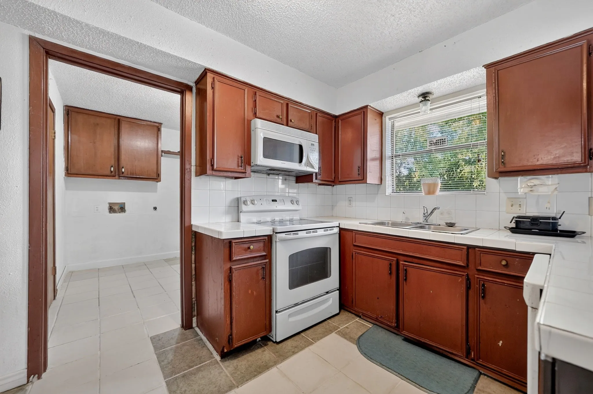 Kitchen featuring wood-finish cabinetry, white tile countertops, and a full suite of white appliances