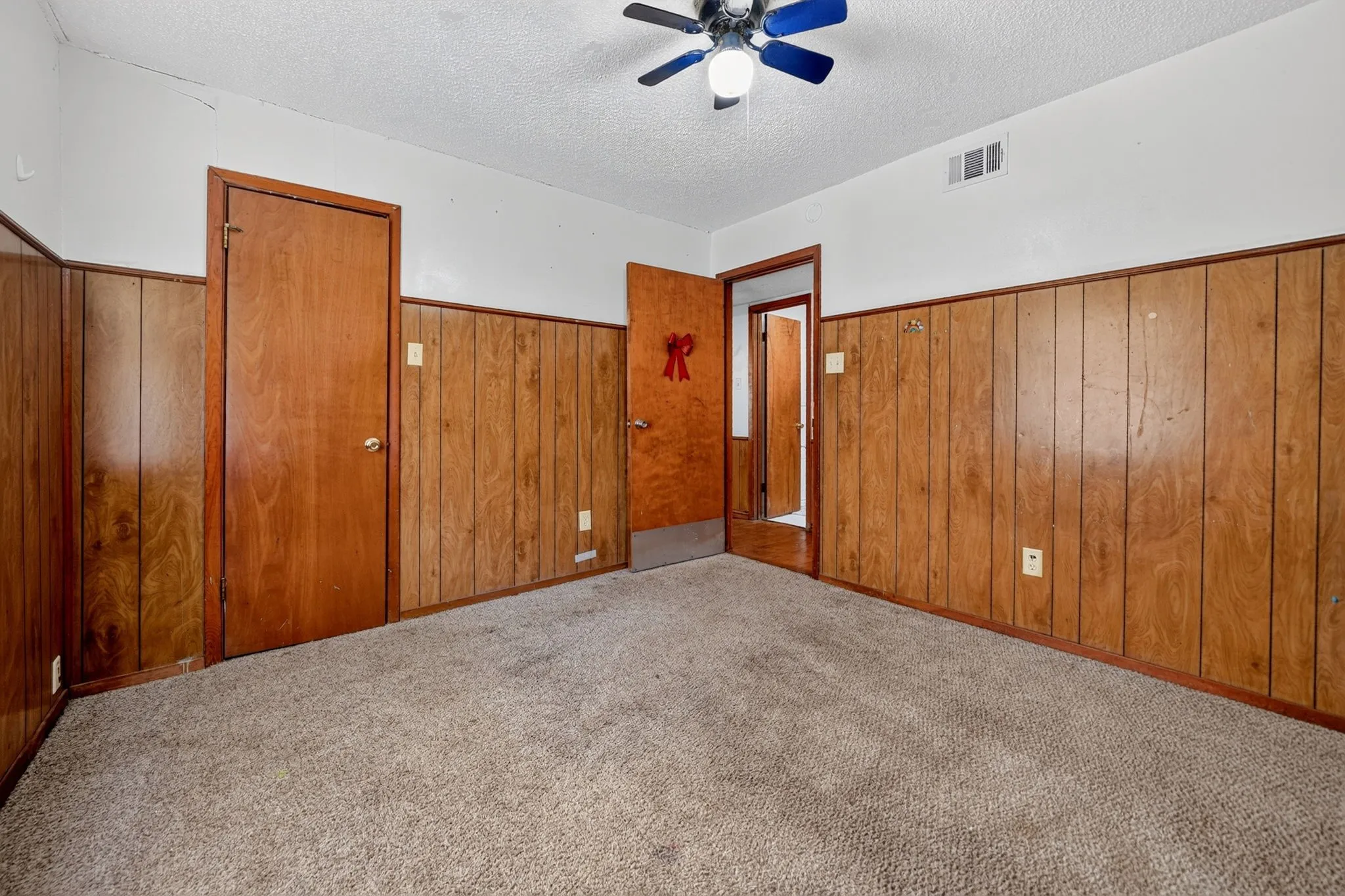 Carpeted flooring, wood paneling, white painted walls, and a ceiling fan with integrated lighting