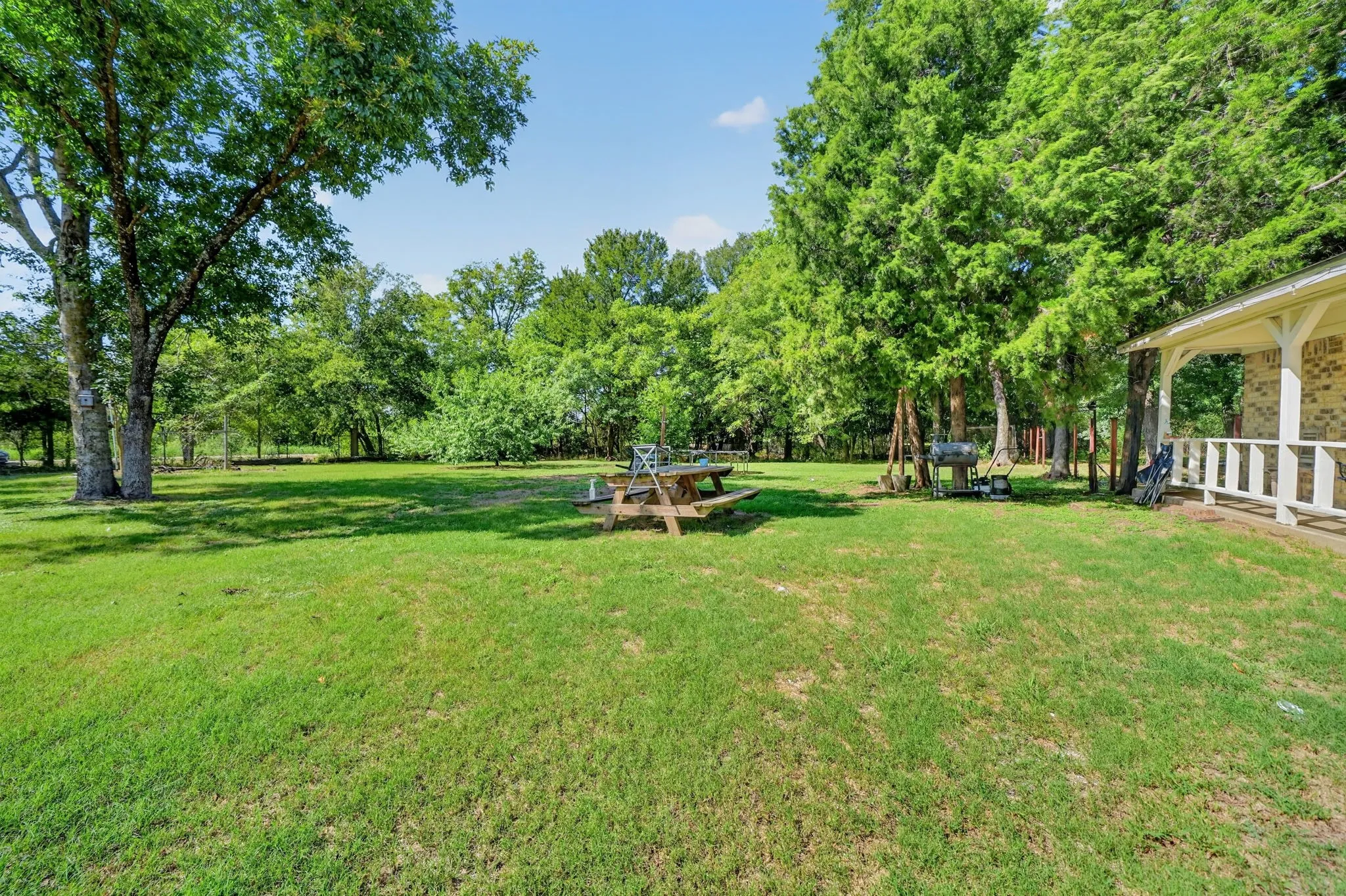 Expansive grassy yard with mature trees and a covered porch featuring white railings
