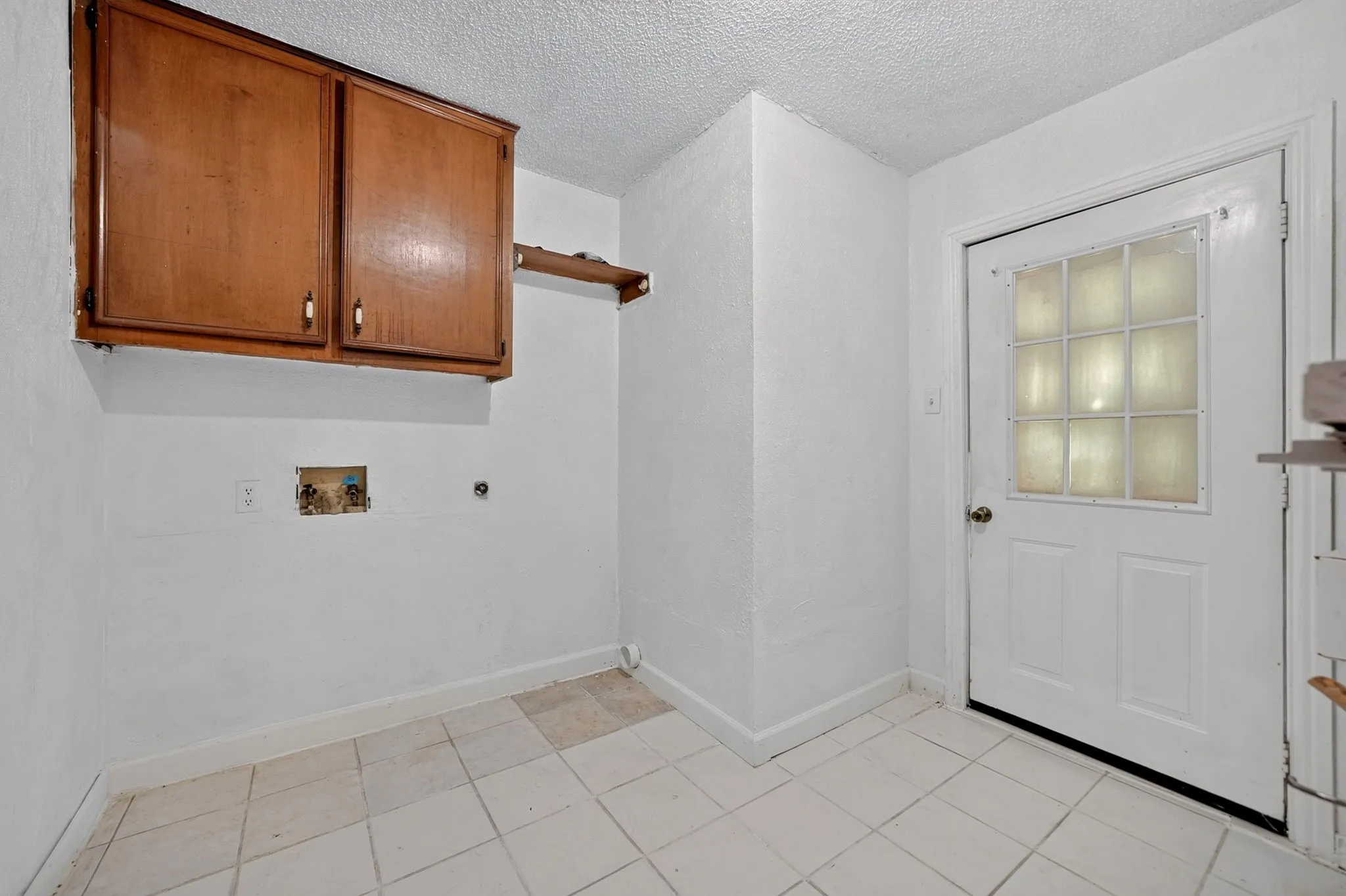 White tile flooring, wood-finish cabinetry, built-in shelving, and a door with glass block inserts