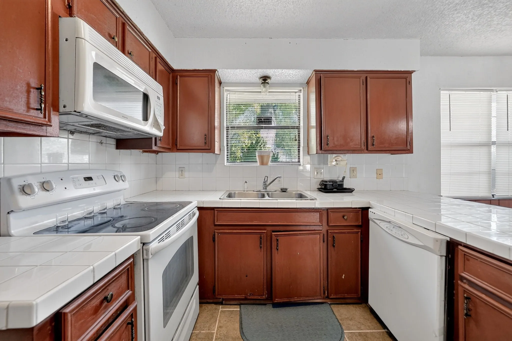 Kitchen with wood-finish cabinetry, white tile countertops, and a white tile backsplash