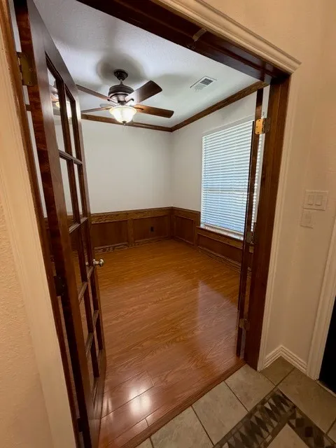 Wood-finish flooring, wood-paneled wainscoting, a ceiling fan with integrated lighting, window blinds, and French doors