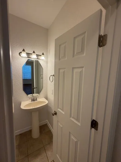 Pedestal sink with chrome-finish faucet, octagonal wall mirror, and three-light vanity fixture