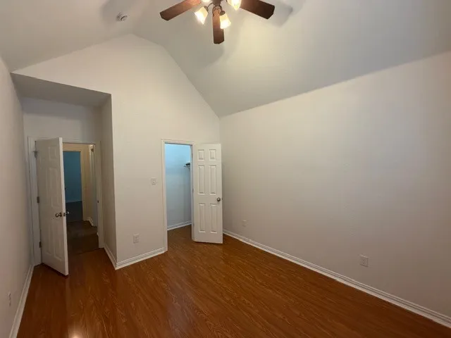 Vaulted ceiling with a ceiling fan, wood-finish flooring, and white interior doors