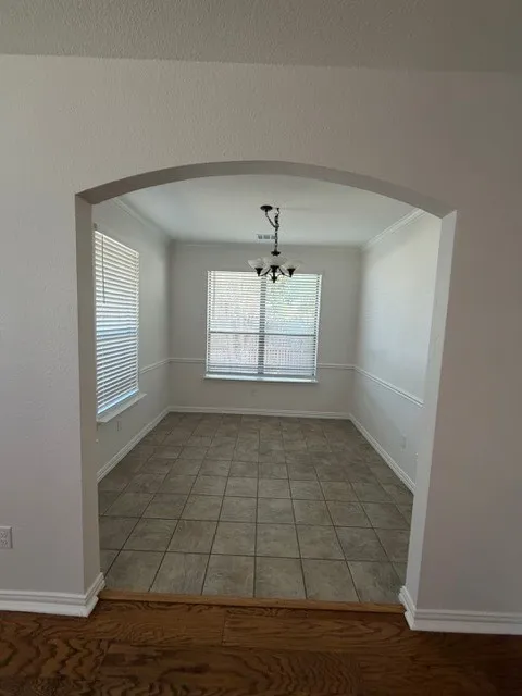 Arched entryway opening to a room with tiled flooring, multiple windows with blinds, wainscoting, and a ceiling-mounted light fixture