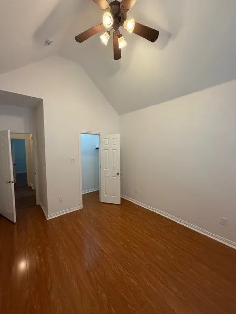 Vaulted ceiling, wood-finish flooring, ceiling fan with integrated lighting, and white paneled doors