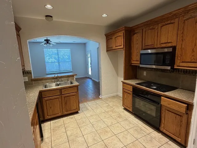 Kitchen featuring tile flooring, wood cabinetry, stainless steel microwave, electric cooktop, and a double basin sink